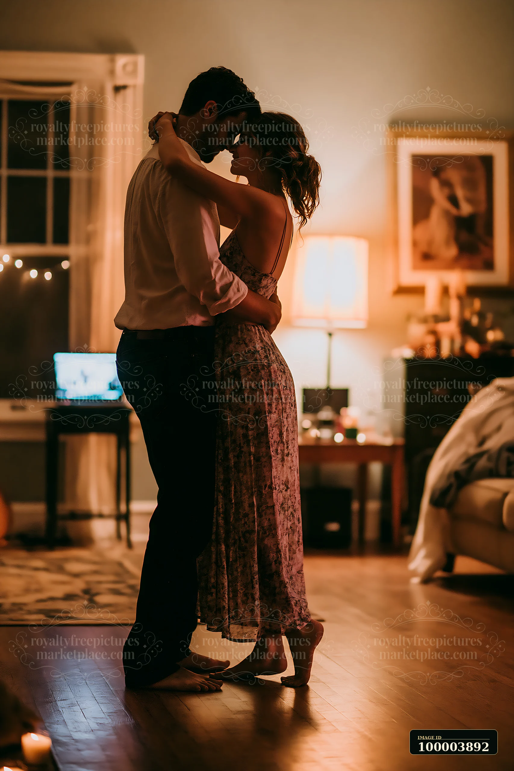 Couple embraces while dancing barefoot on a wooden floor in a warmly lit living room.