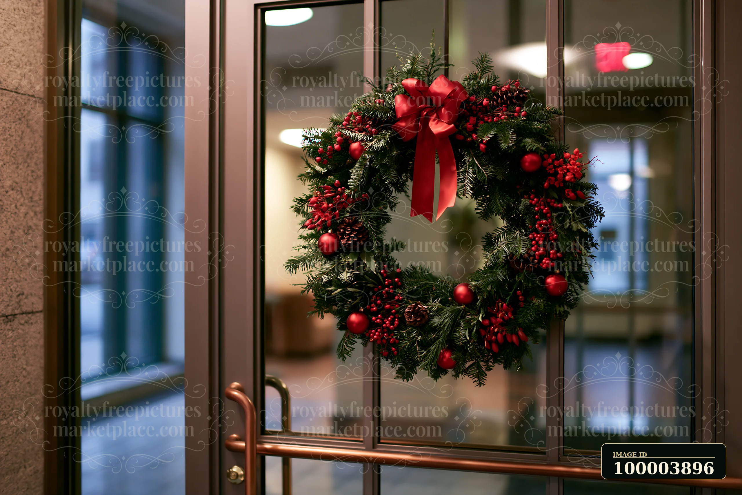 A Christmas wreath decorated with red ornaments and a bow hangs on an apartment door in a well-lit indoor setting.