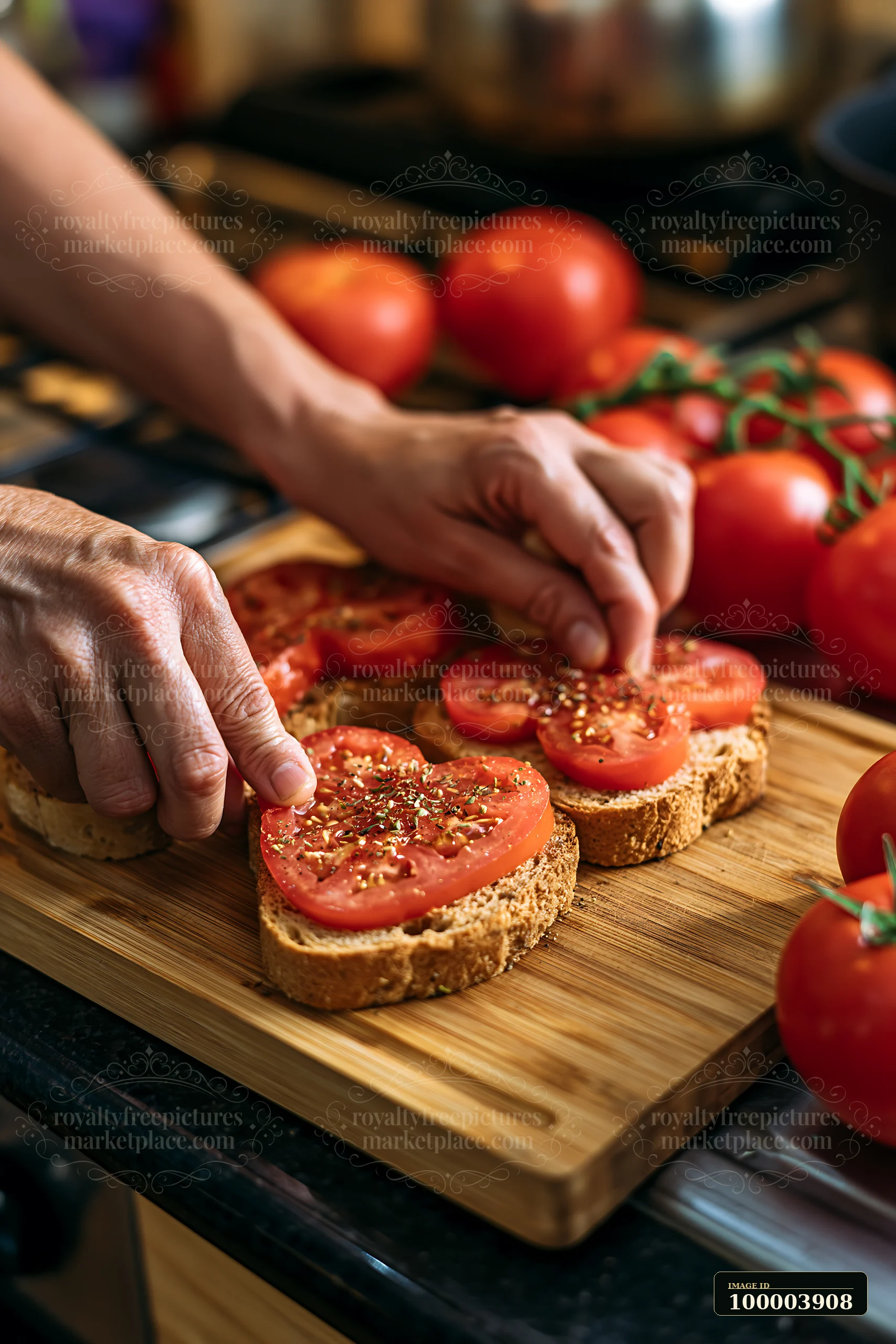 Hands arrange seasoned tomato slices on bread on a wooden cutting board in a warmly lit kitchen.