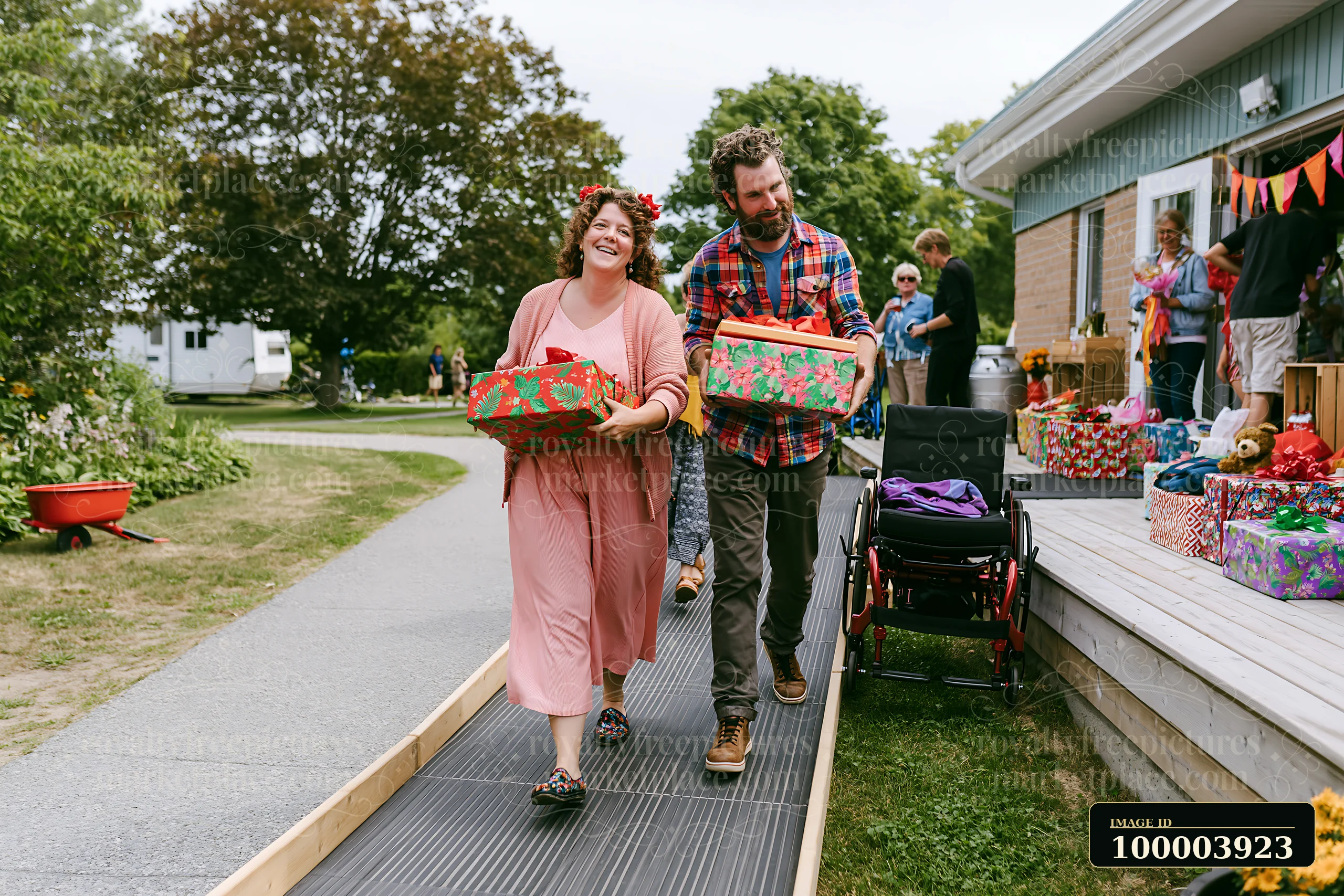 A woman and a man carry decorated gift boxes while walking on a path outside a building.