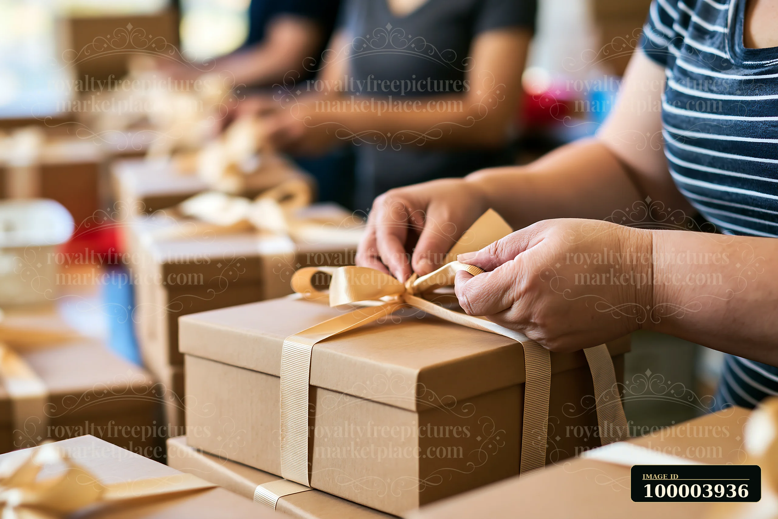 Hands are tying a ribbon around a gift box in a busy packing area filled with other wrapped boxes.
