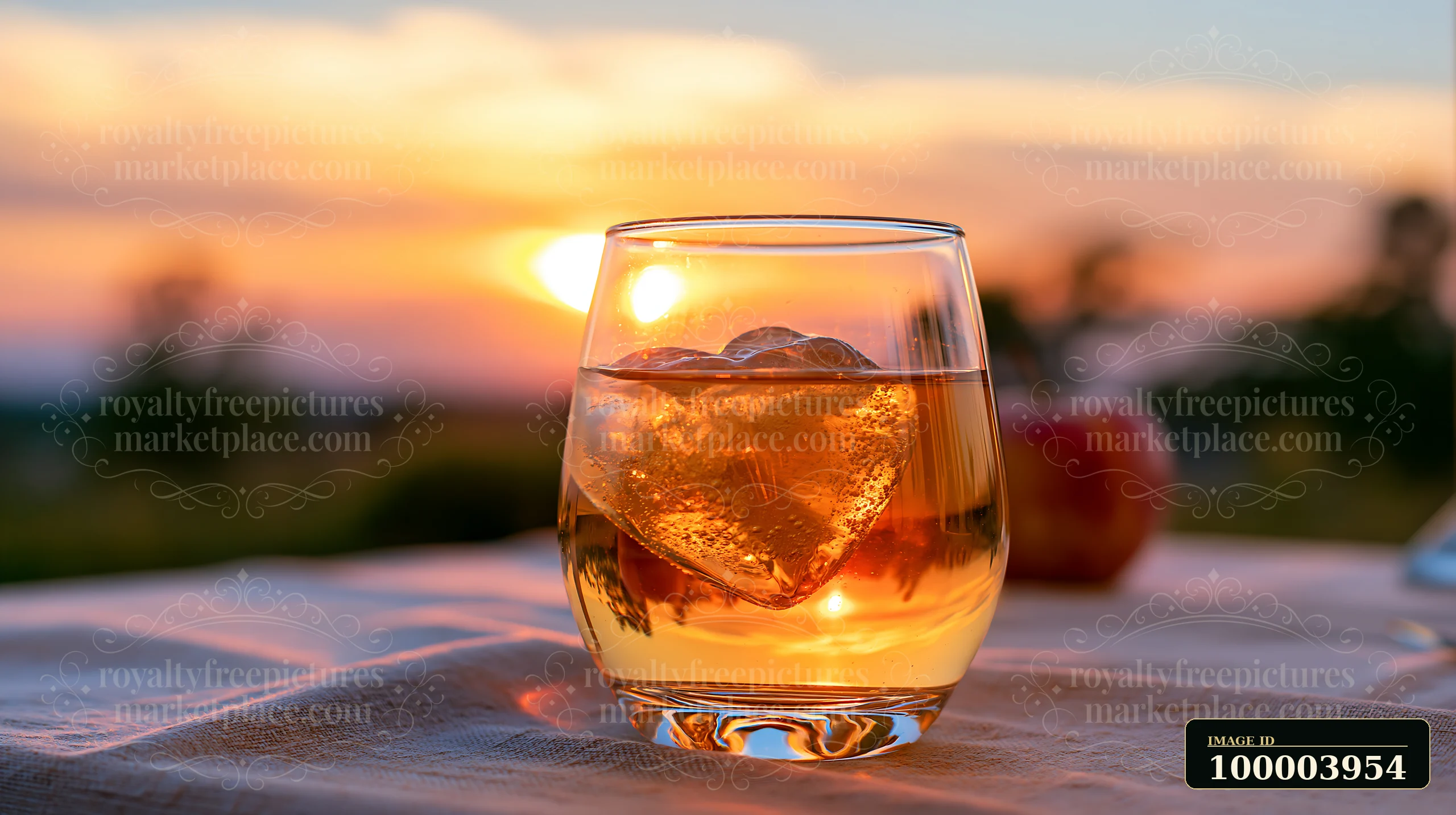 A heart-shaped ice cube melts in a drink placed on a table during sunset.