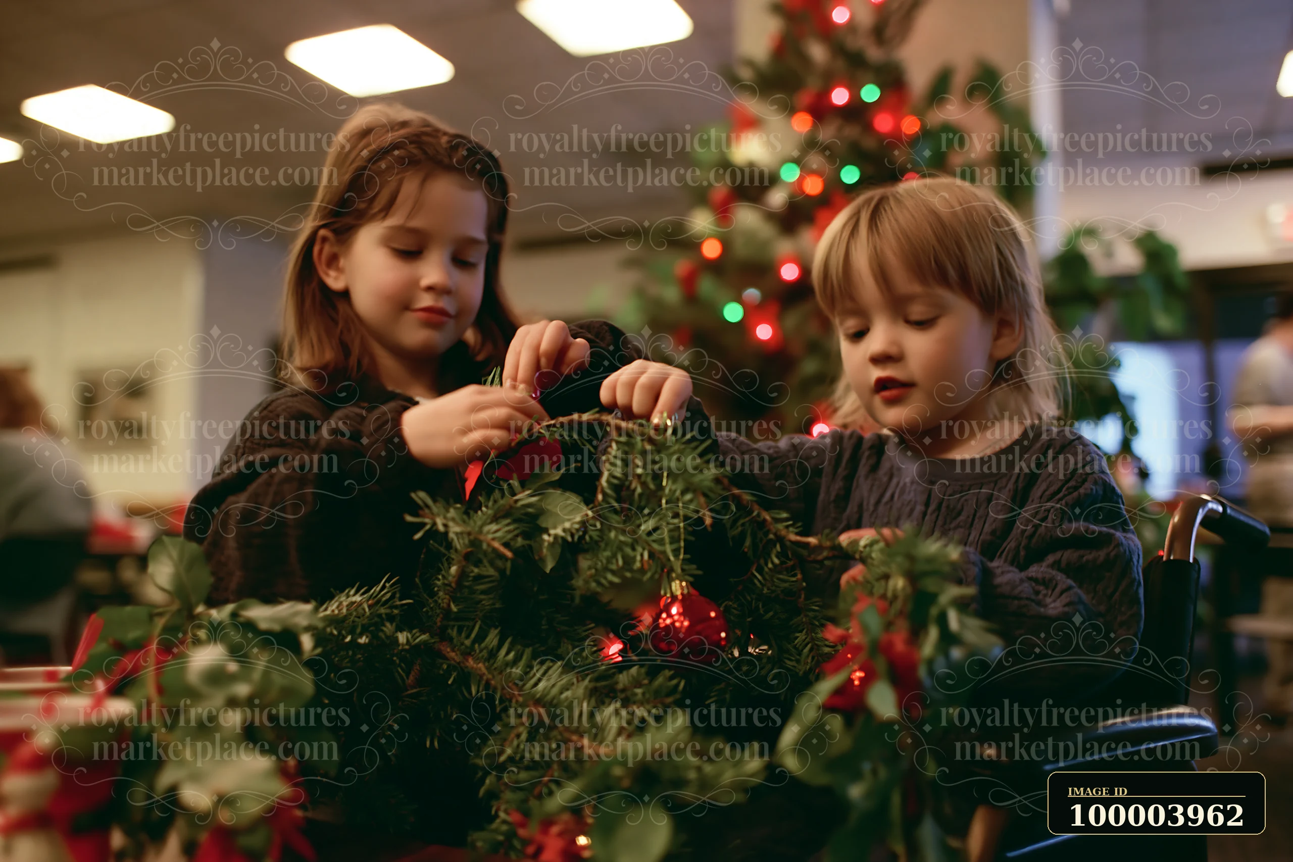 Two children decorate evergreen branches with red ornaments indoors beside a lit Christmas tree.