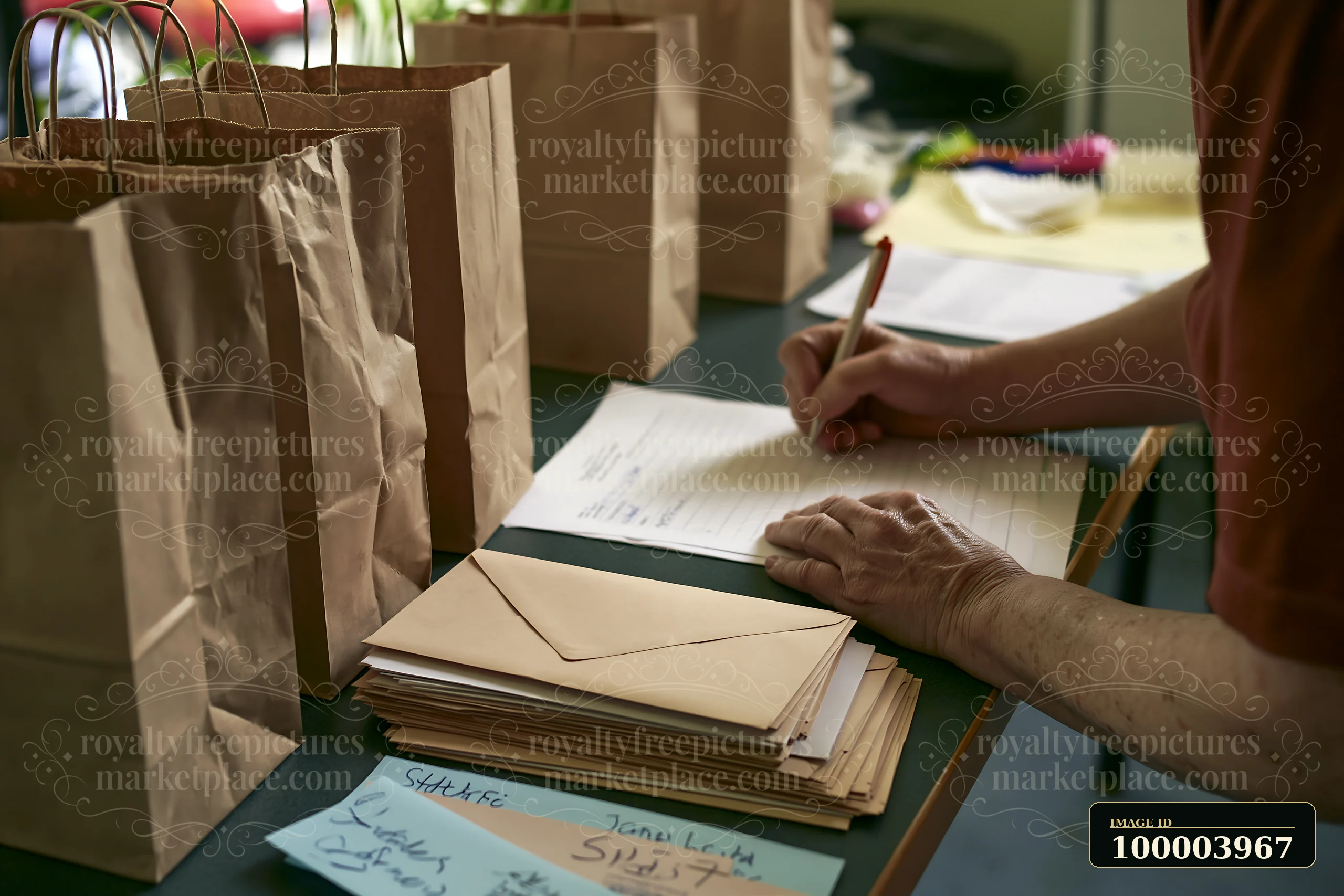A person writes a gift list at a desk surrounded by paper bags and envelopes.