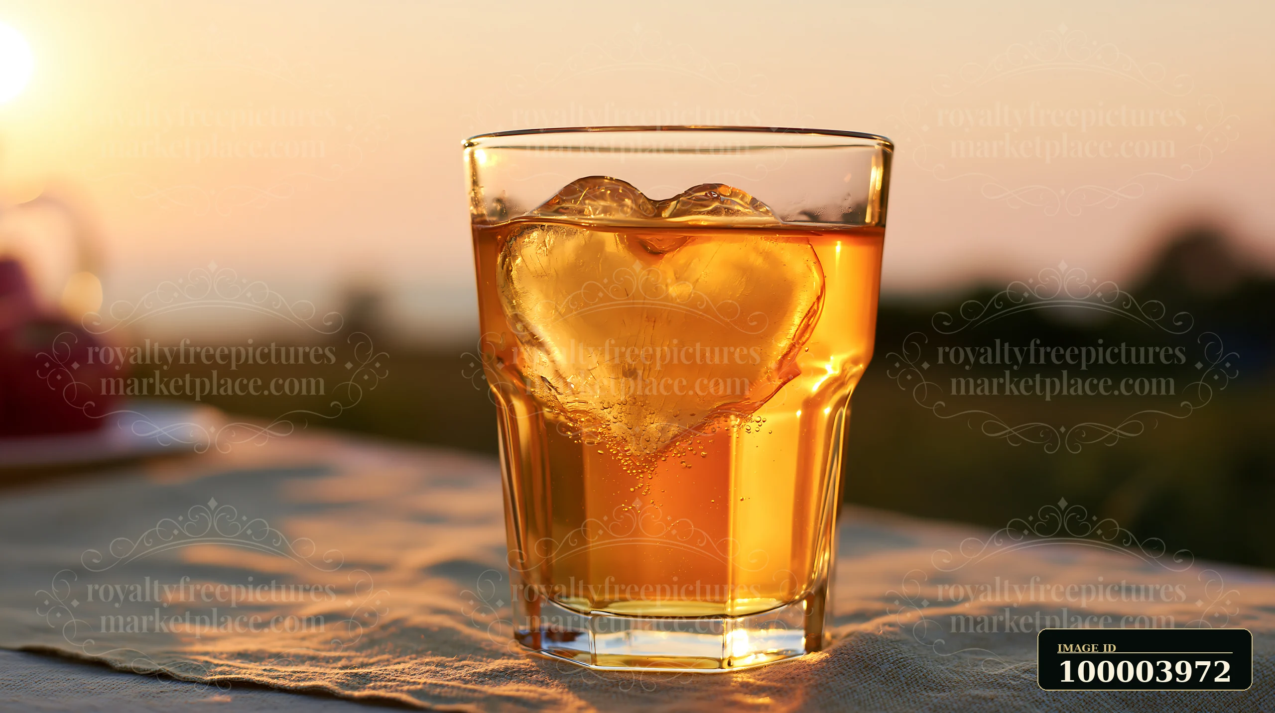 A heart-shaped ice cube is melting in a glass of tea at a sunset gathering.
