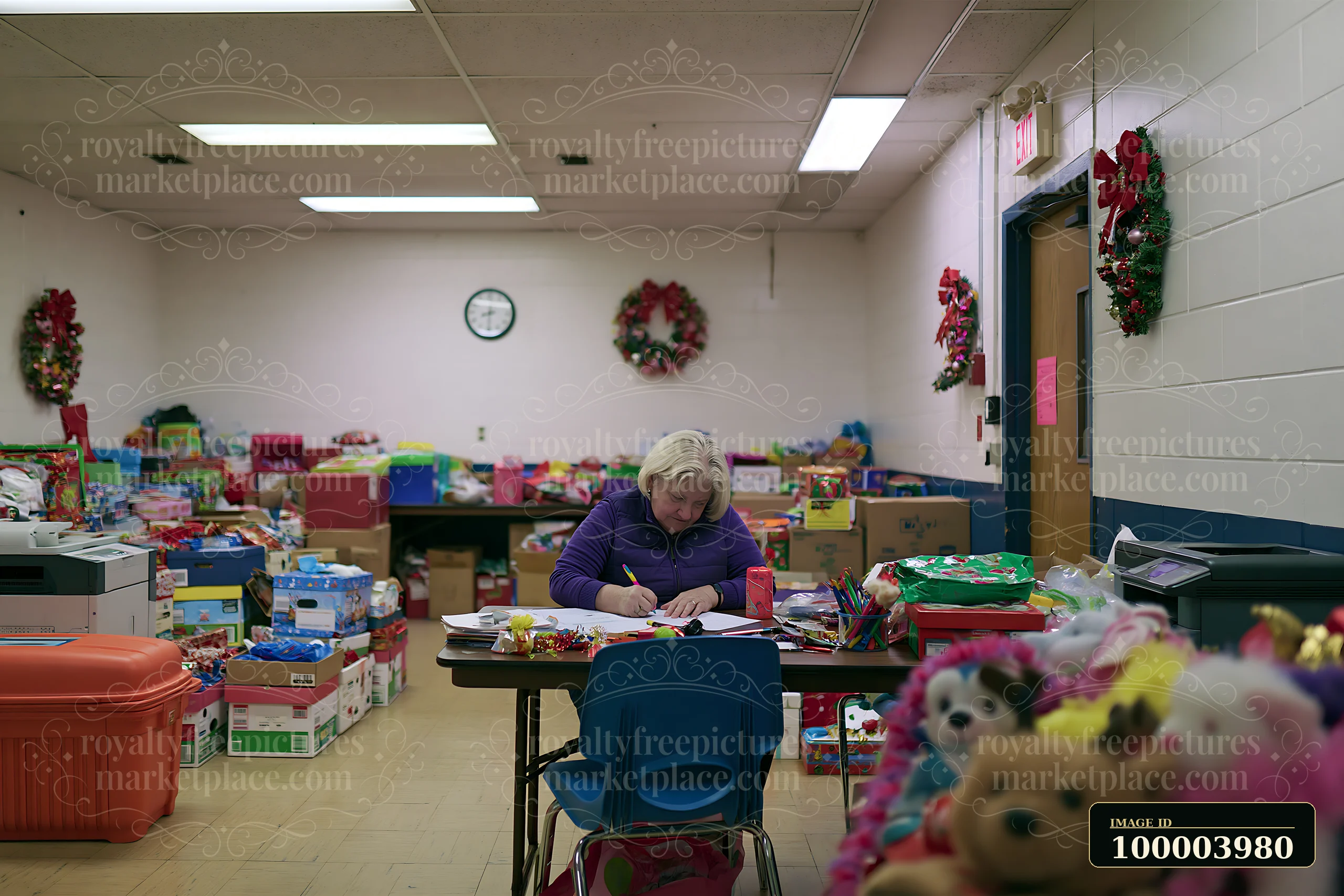 A person is writing a gift list at a desk surrounded by boxes of gifts and holiday decorations.