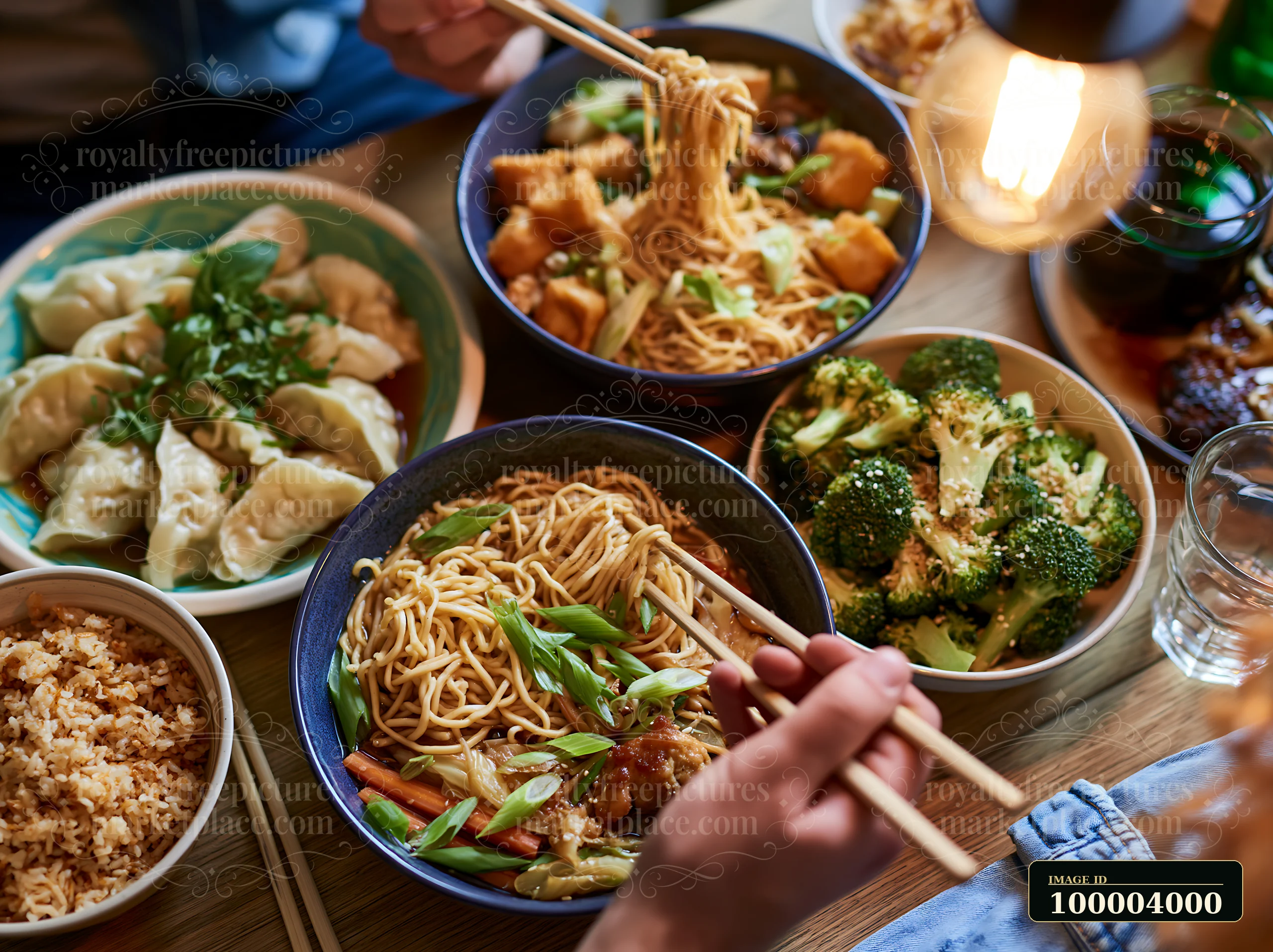 A family shares a meal with bowls of noodles, dumplings, broccoli, and rice on a wooden table.