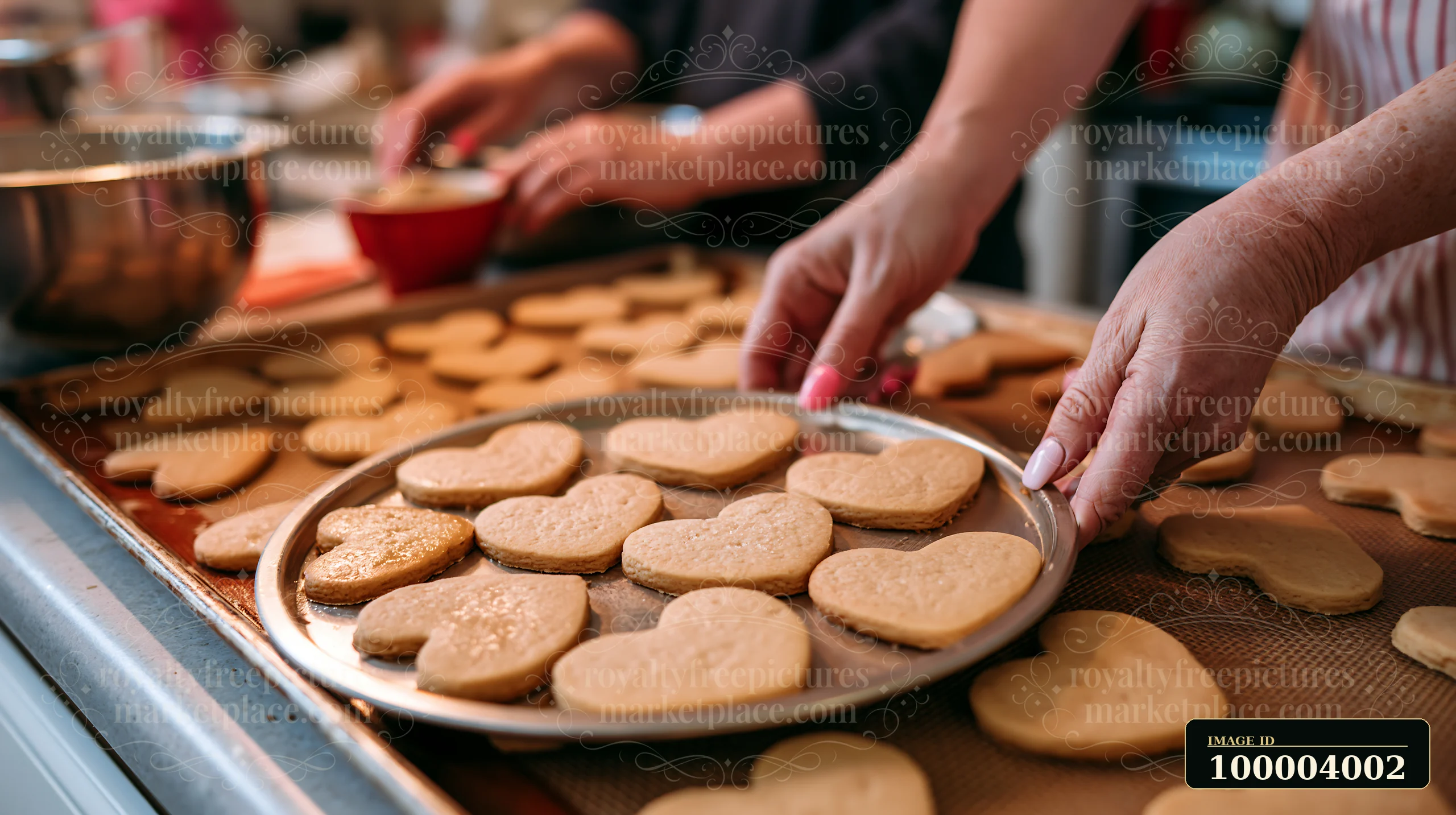 Heart-shaped cookies fill baking trays as two people arrange them on a kitchen counter.