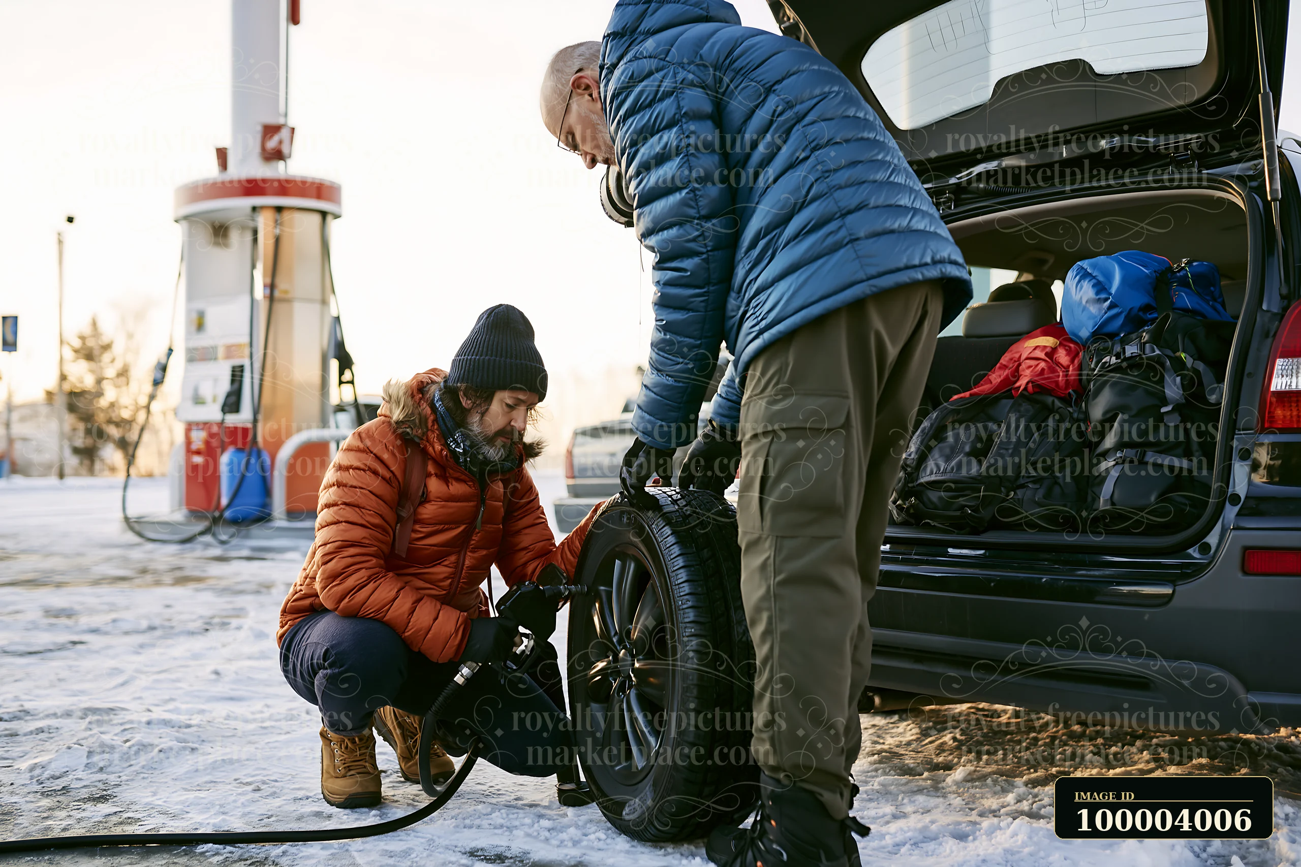 Two men are fixing a car tire at a gas station on a winter day.