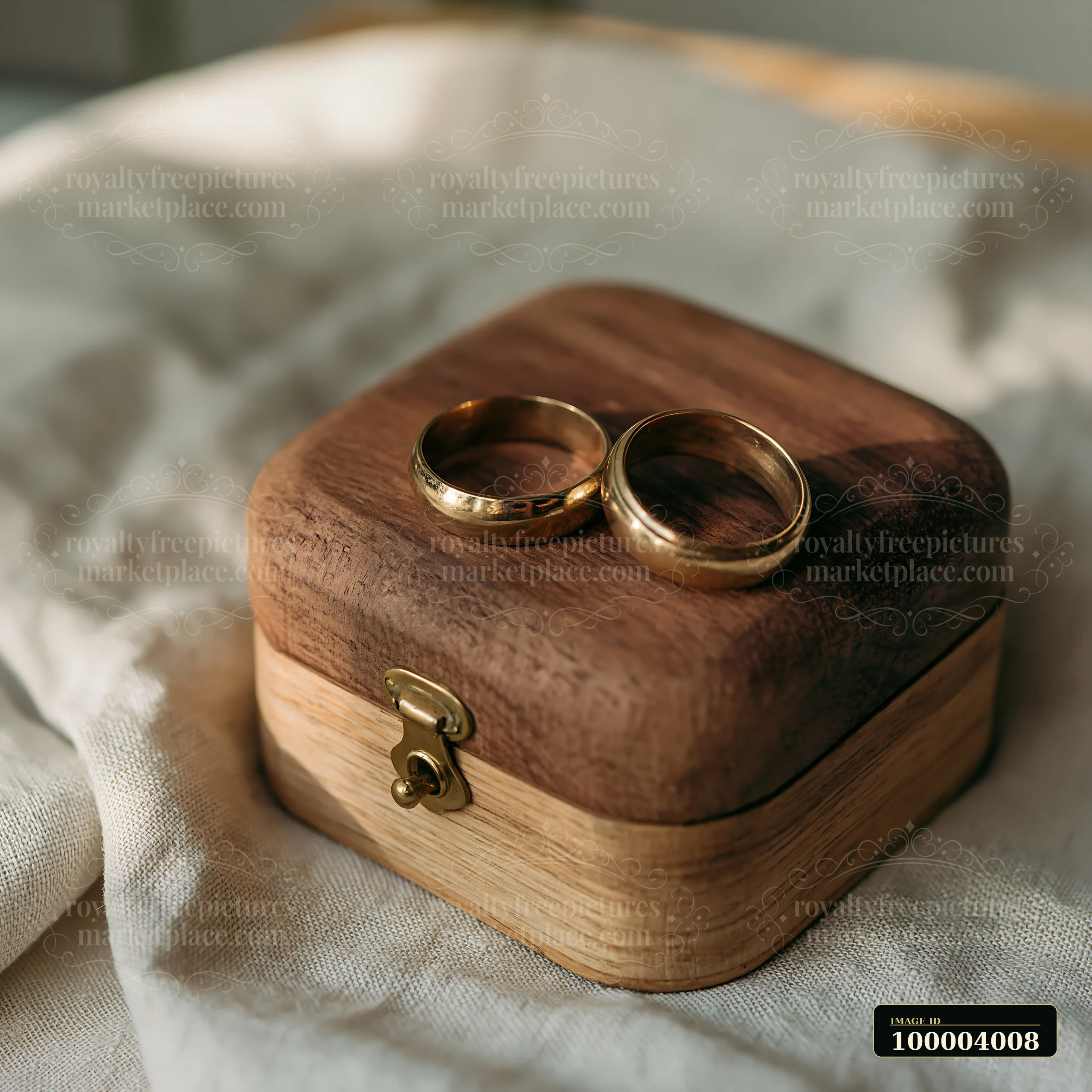 Two gold wedding rings rest on a wooden keepsake box over rumpled linen in soft morning light.