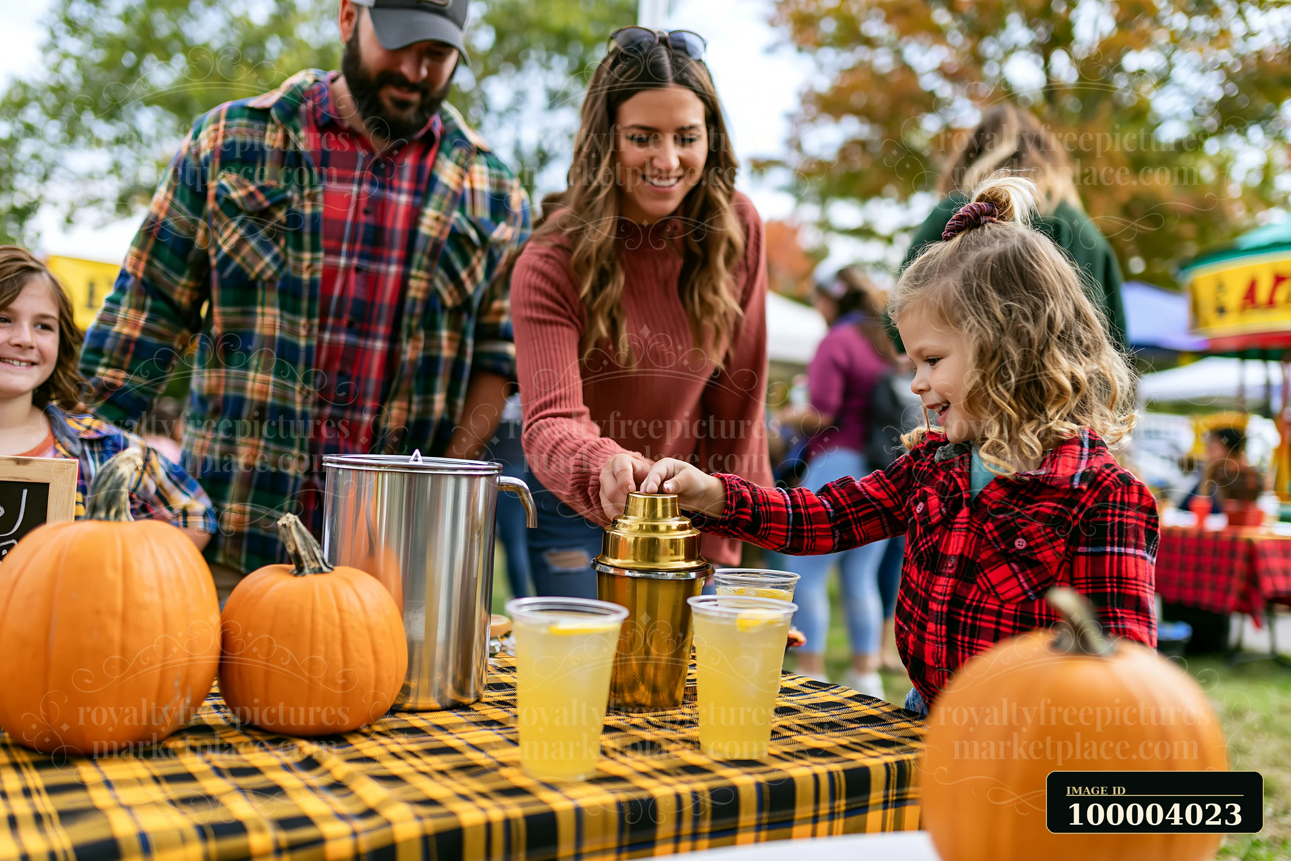 A family shares lemonade at an outdoor festival near pumpkins.