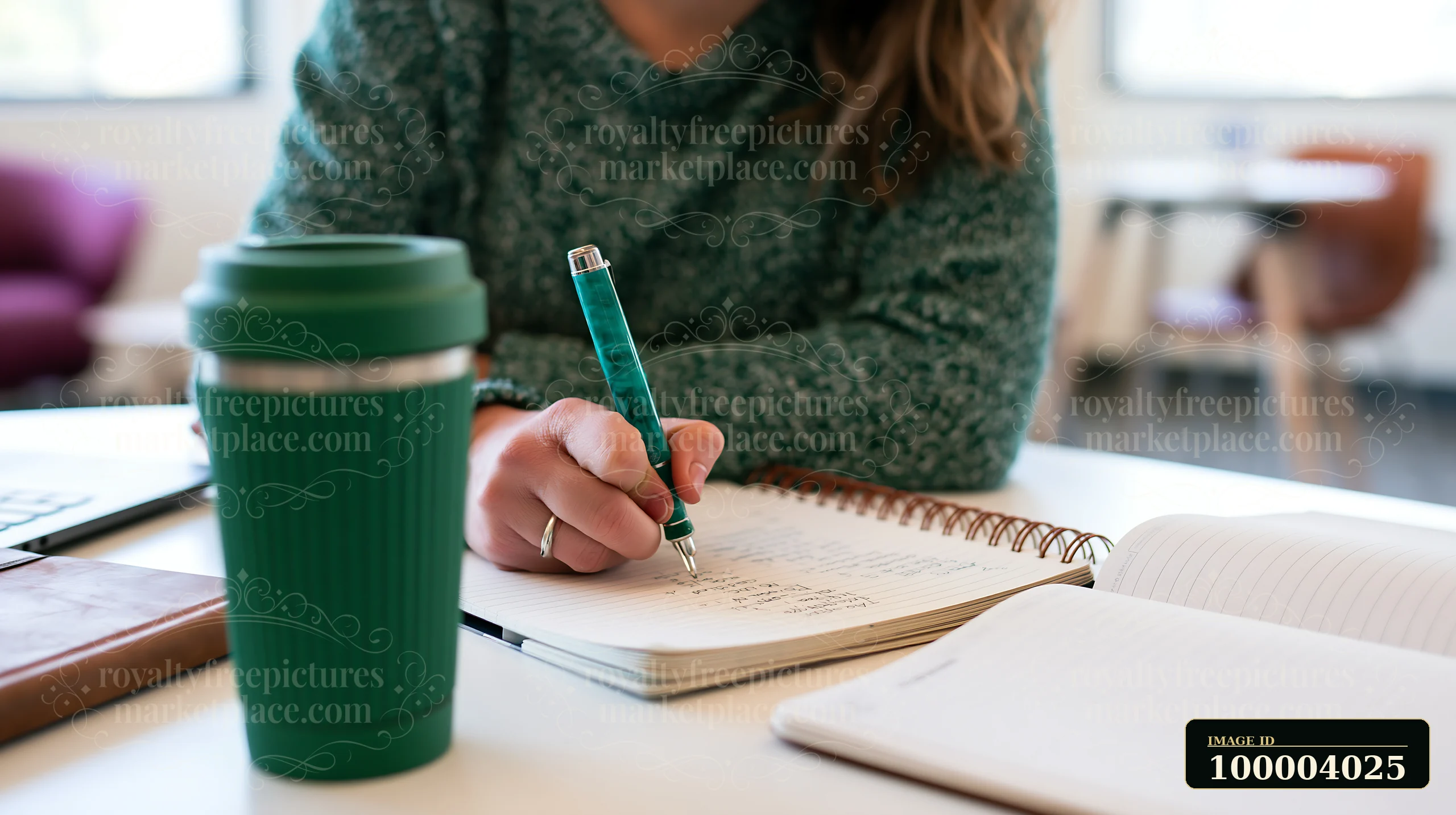 Person writes a gift list in a spiral notebook at a desk beside a reusable travel cup.