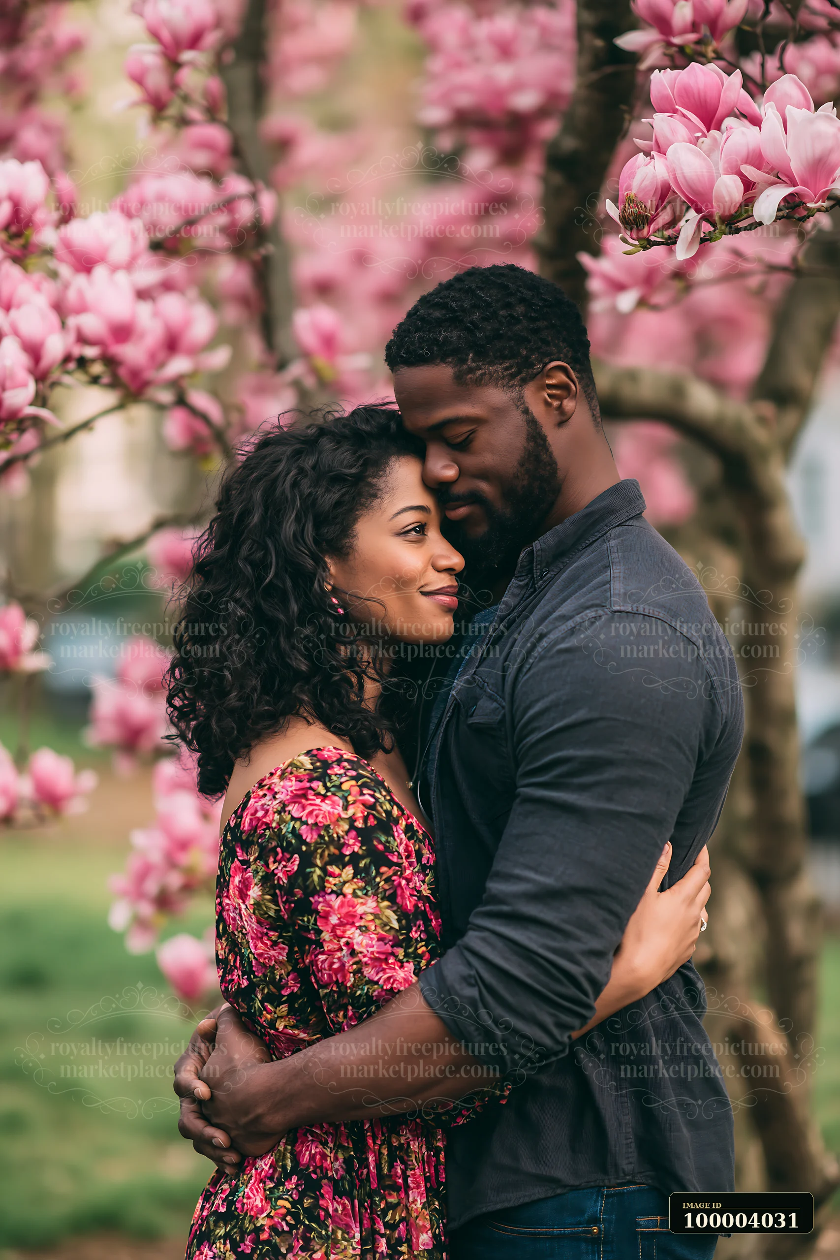 A couple embraces among pink magnolia flowers in a park during spring.