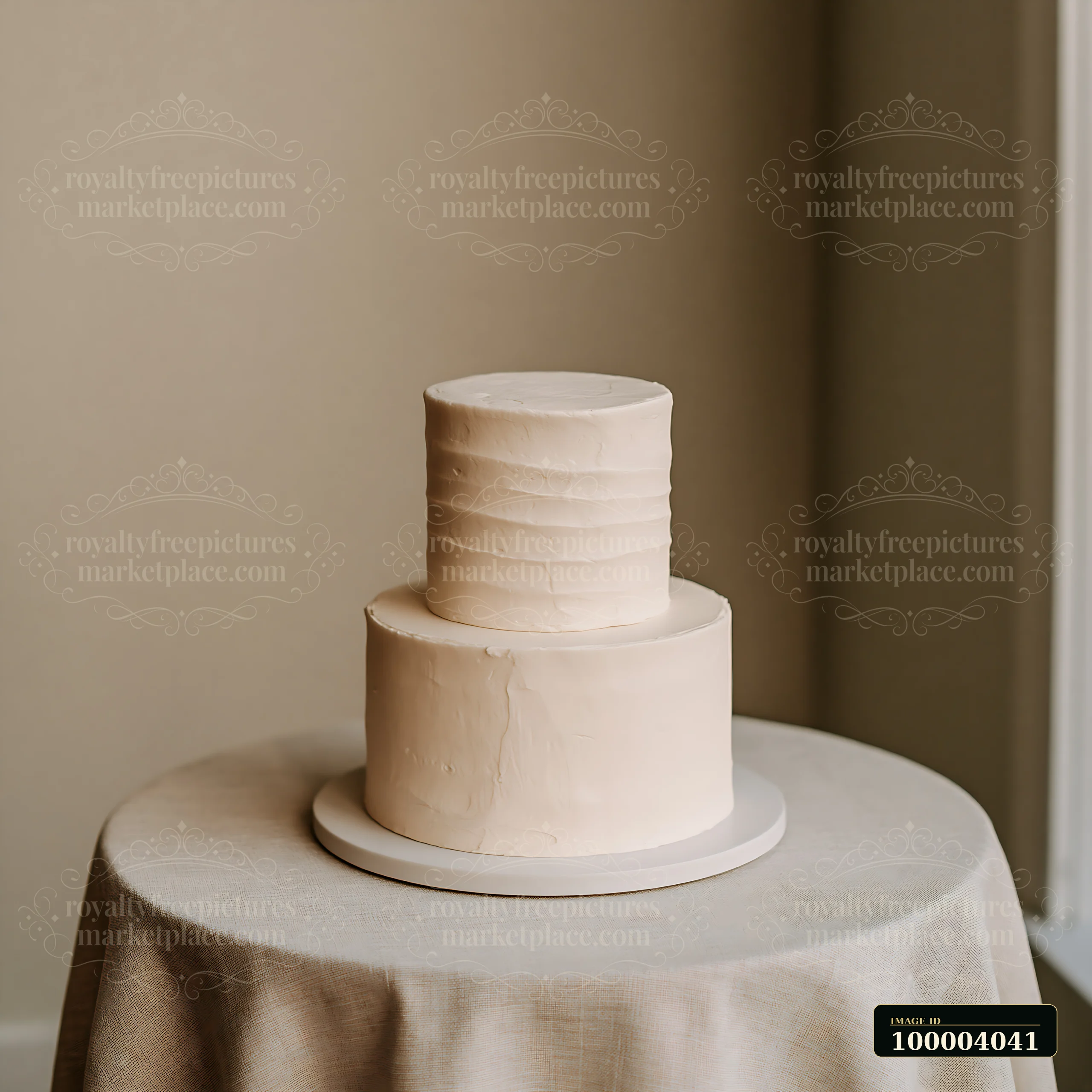 Two-tier white wedding cake on a round stand atop a draped table against a warm neutral background.