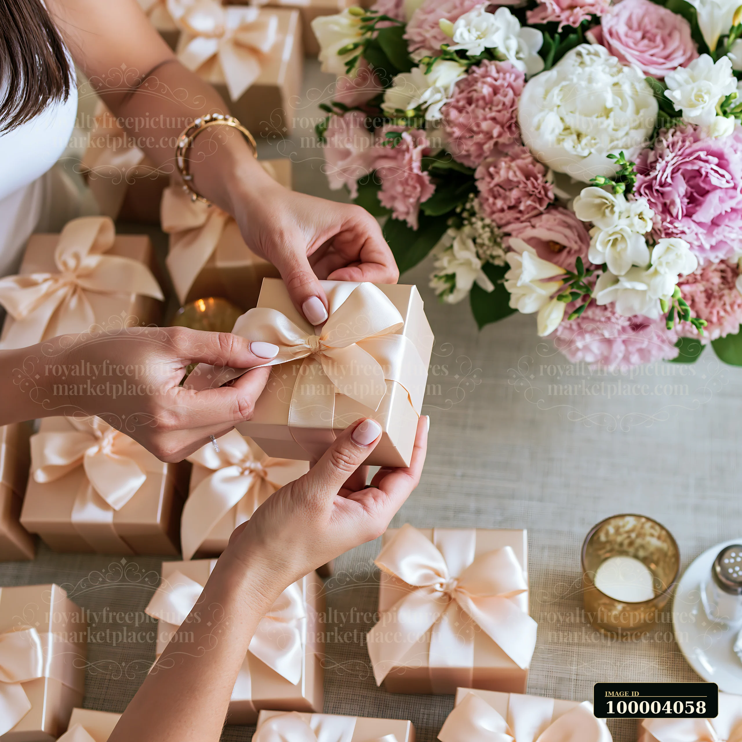 Hands tie a satin ribbon around a gift box beside wrapped presents and a pastel flower arrangement.