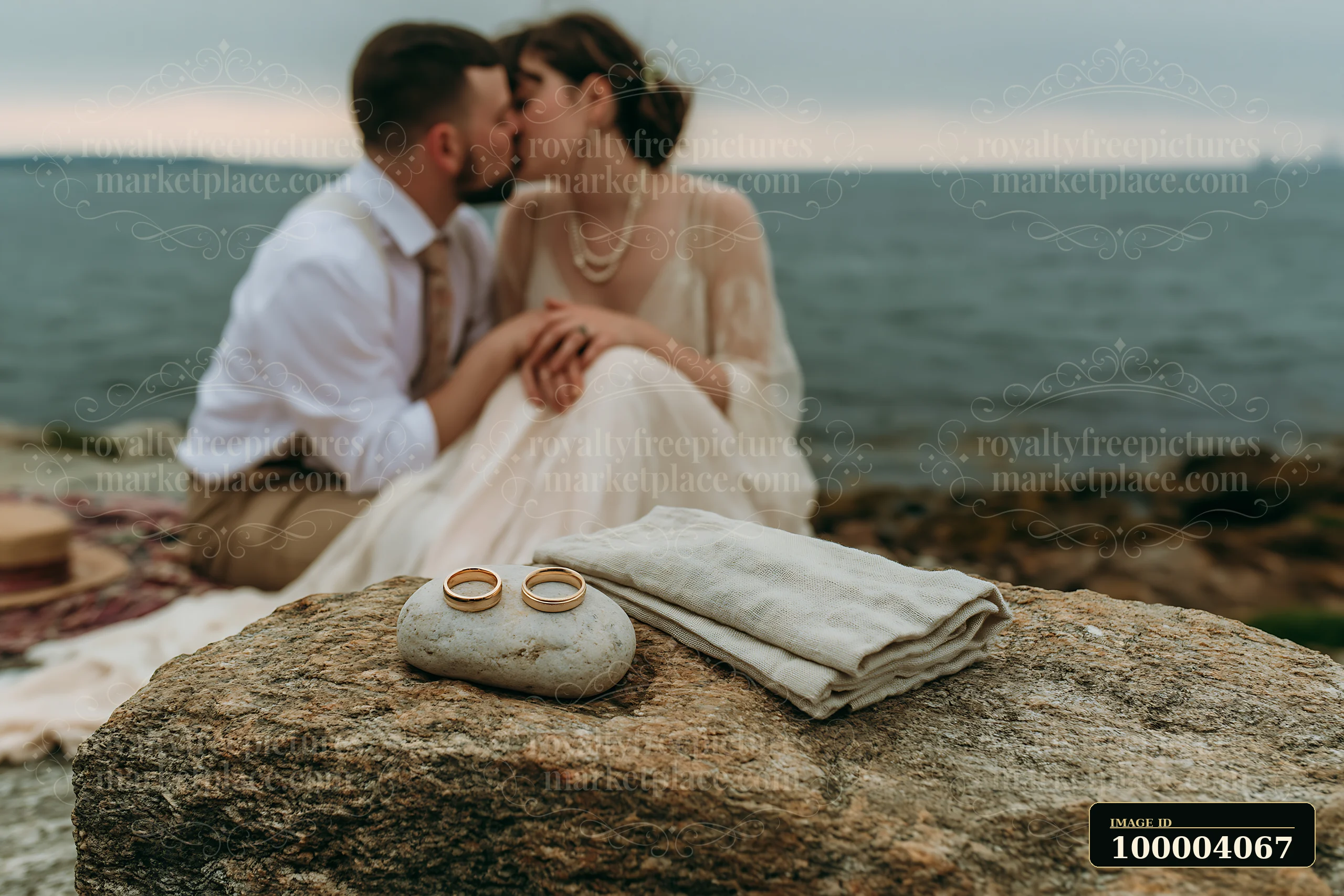 Couple kisses beside wedding rings placed on a stone by the sea.