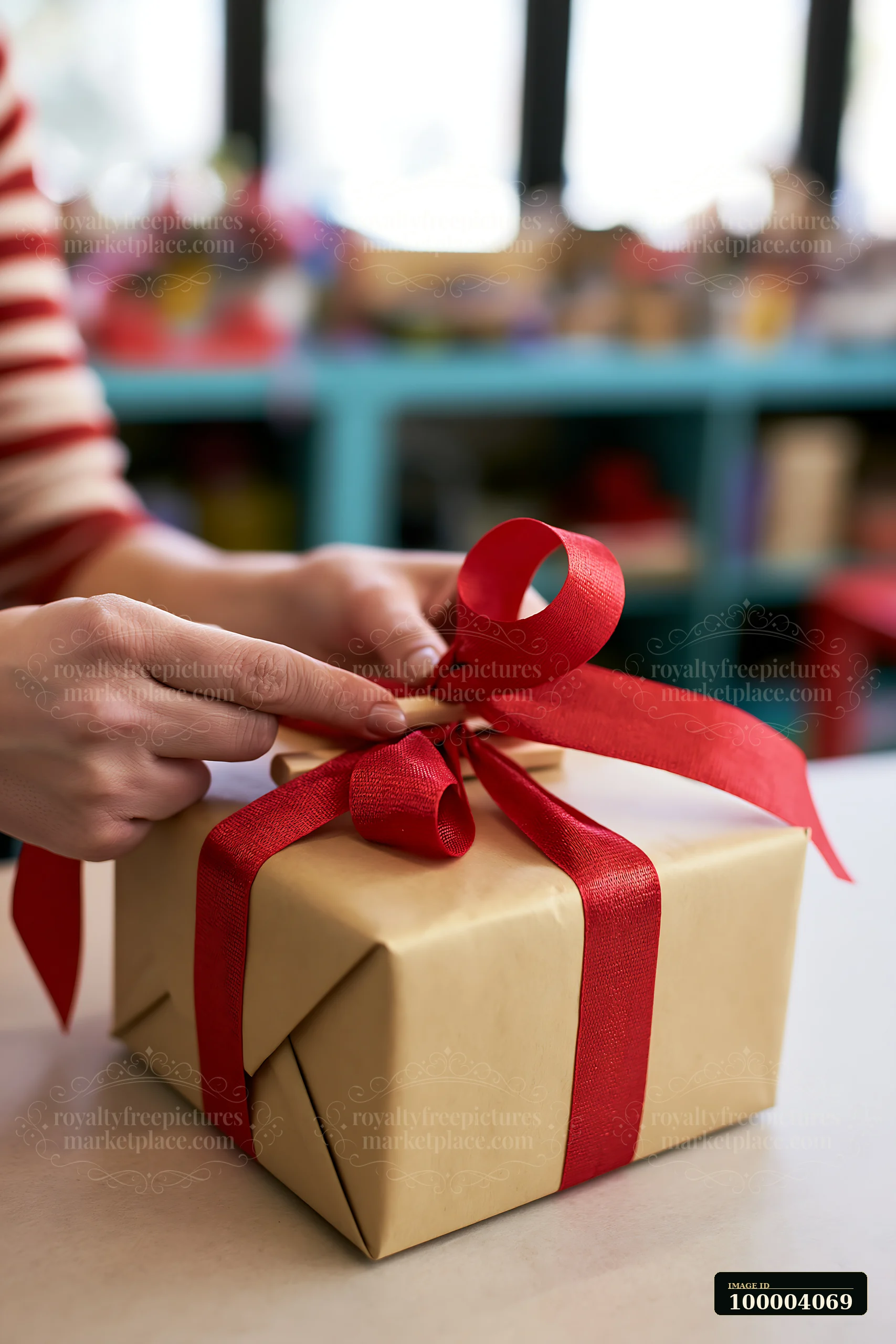 Hands tie a red ribbon around a wrapped gift box on a tabletop.