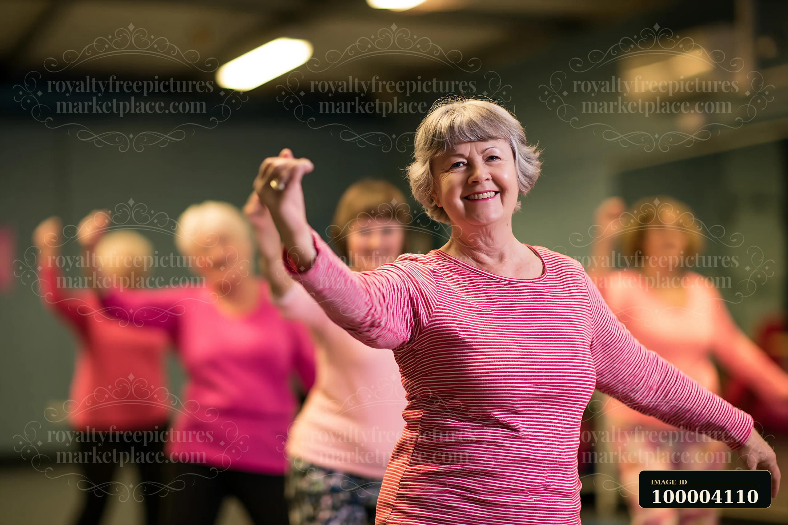 Smiling senior woman raises her arms while women practice dance fitness in a warmly lit studio.