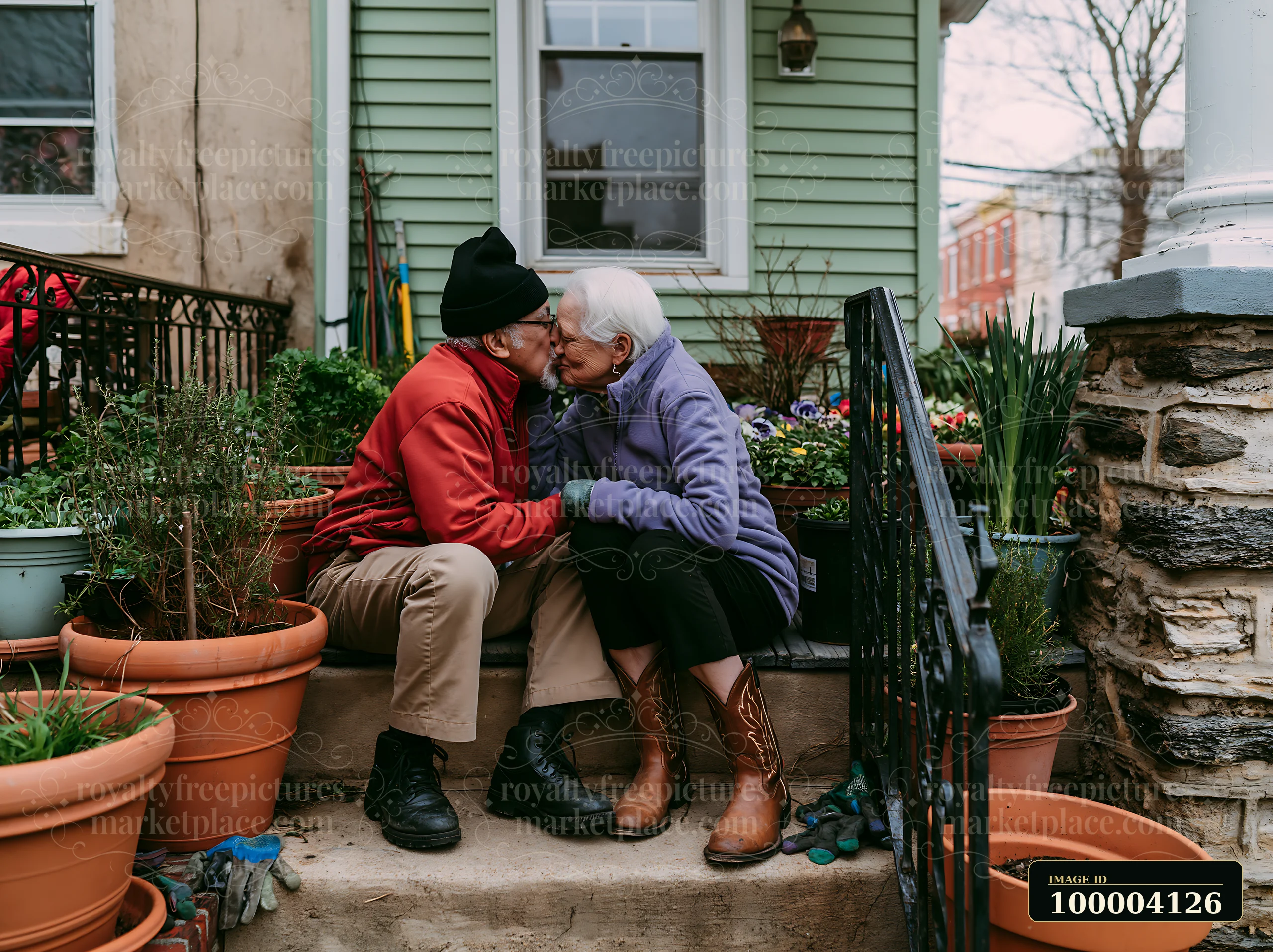 Elderly partners share a kiss on a porch surrounded by potted plants and flowers.