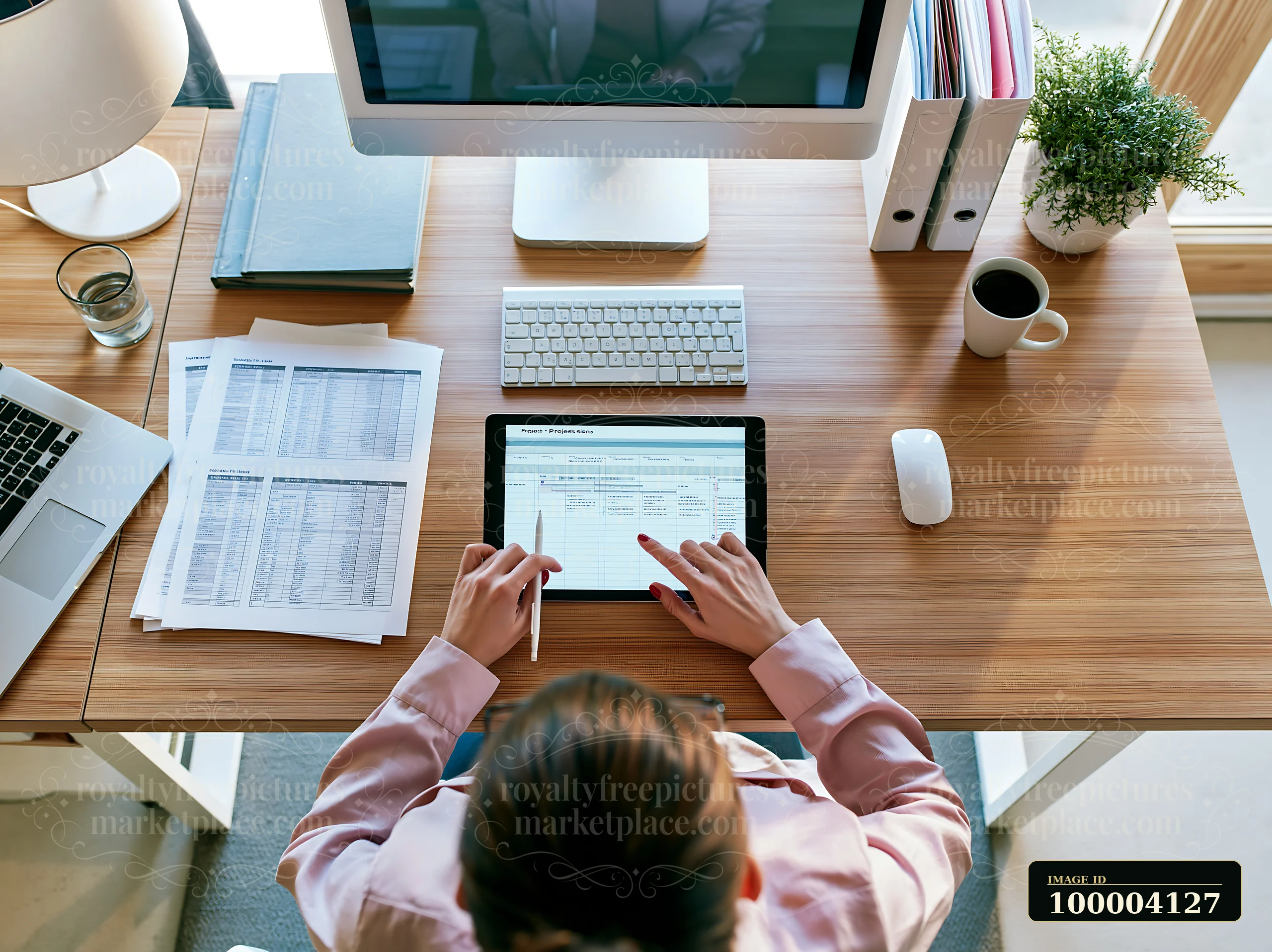 A businesswoman manages a project timeline using a tablet while seated at a wooden desk.