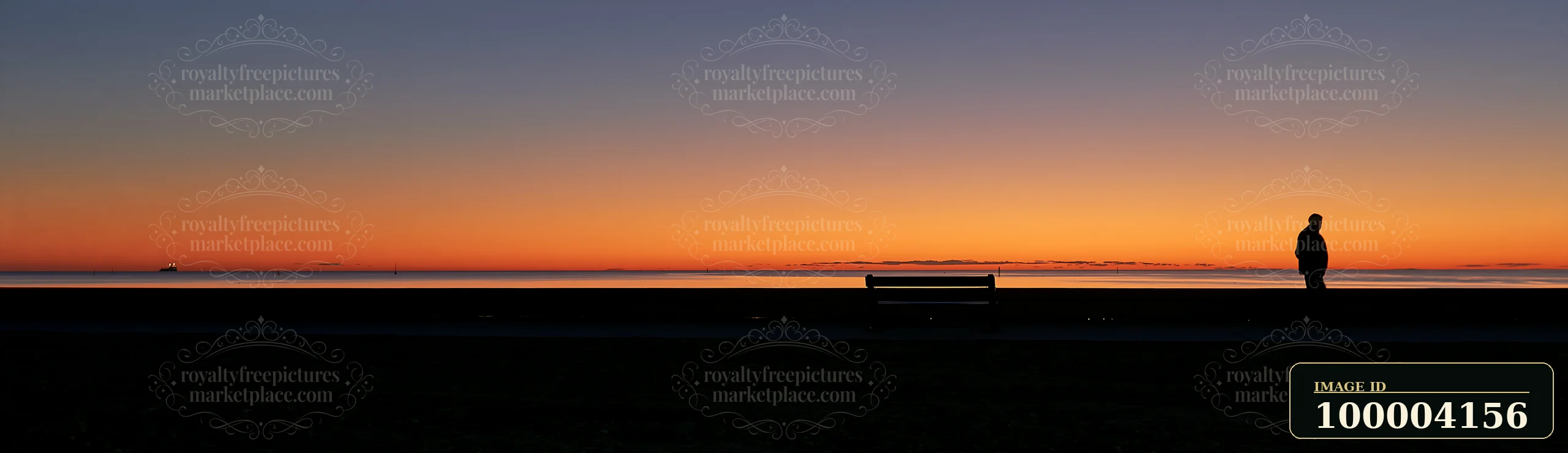 A silhouetted person stands beside a bench overlooking calm water beneath an orange and purple sunset sky.