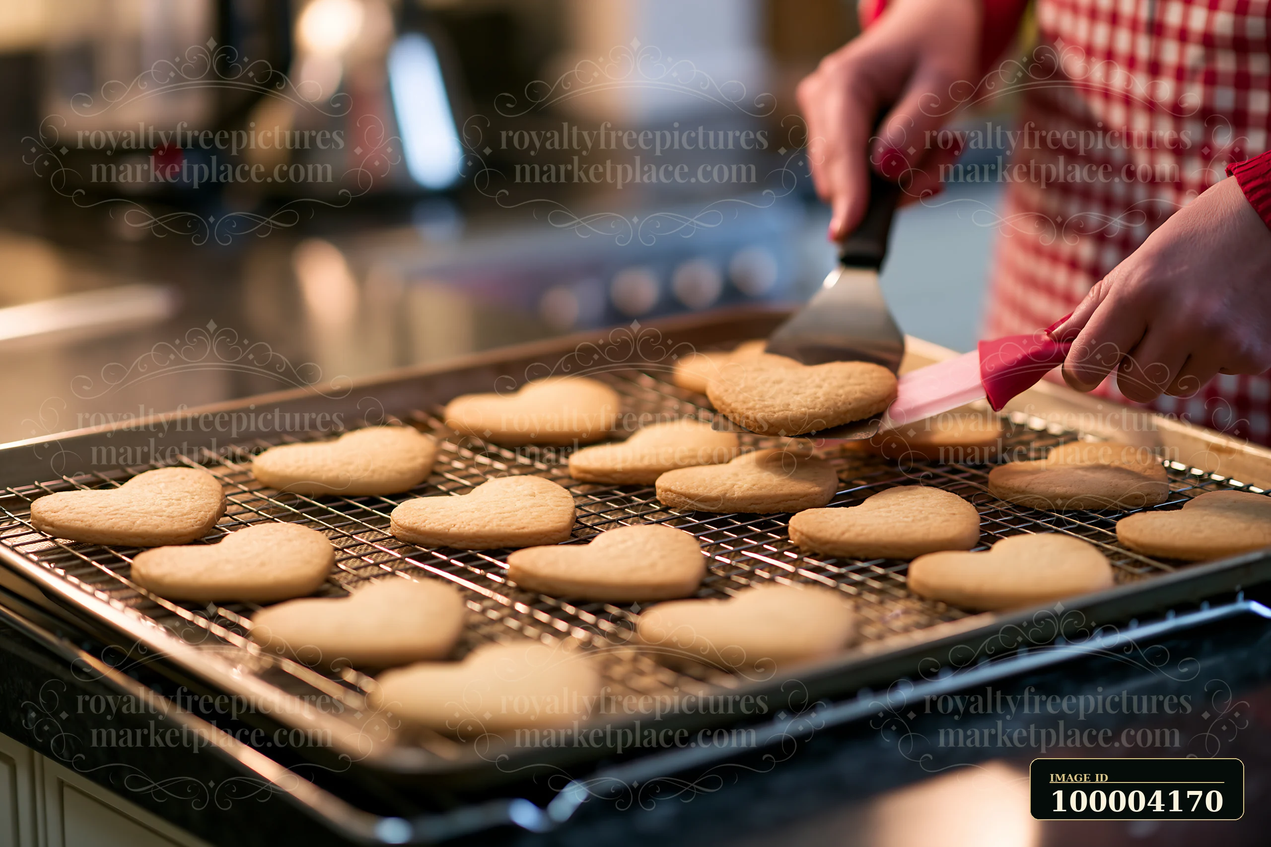 Heart-shaped cookies cool on a wire rack as a person lifts one with a spatula in a kitchen.