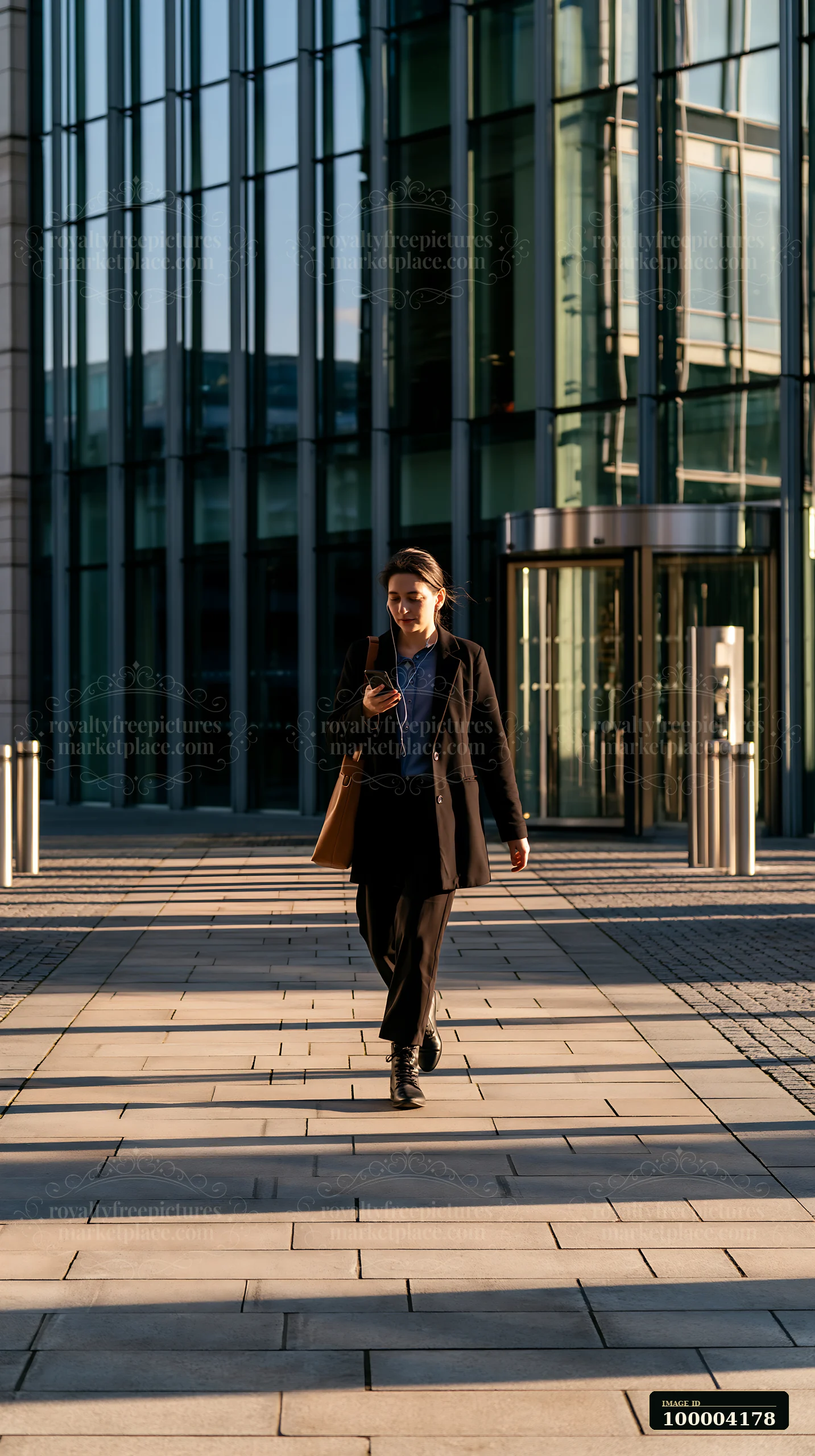 A businesswoman is walking outside an office building while using her smartphone.