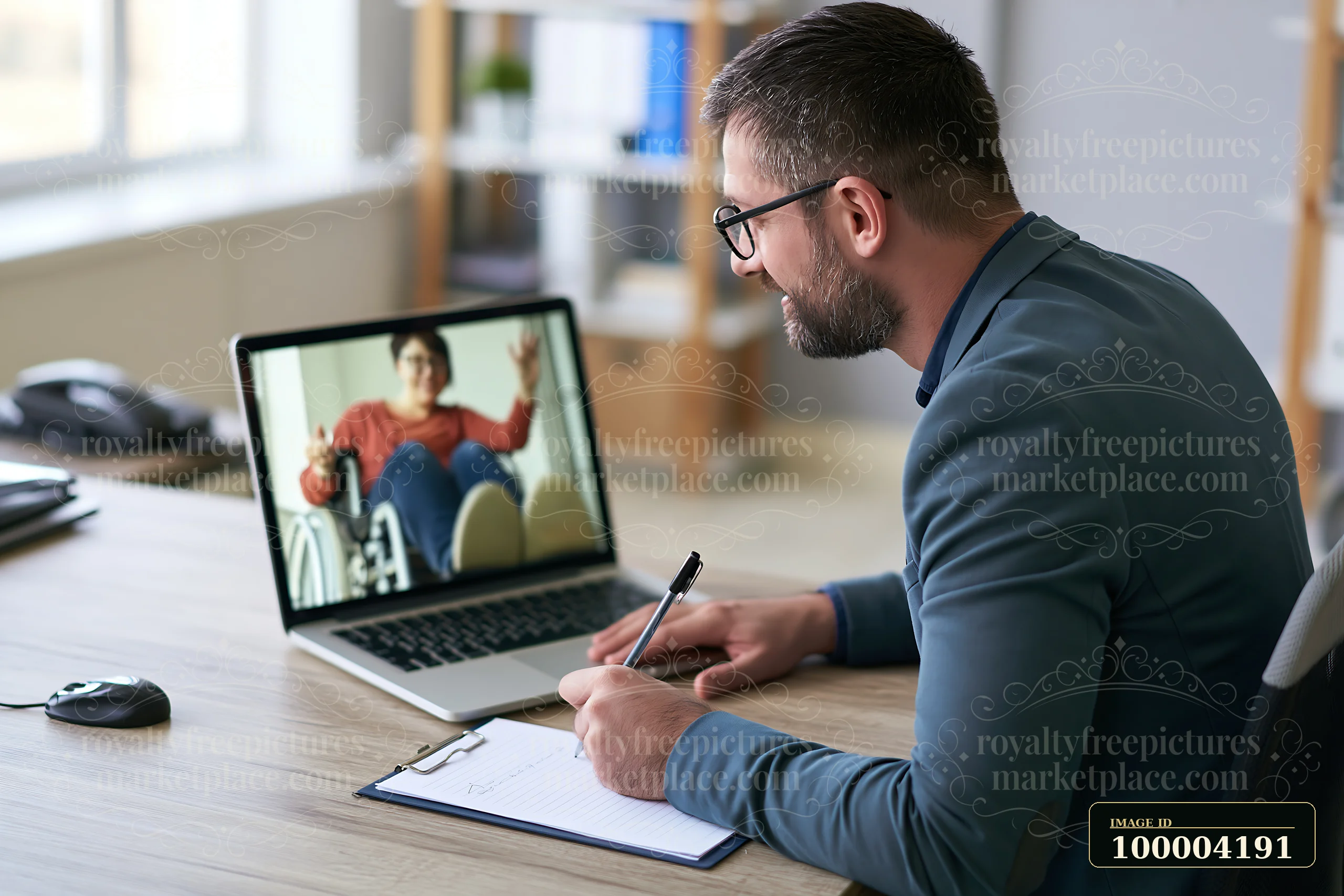 Businessman takes notes while conducting a remote interview online with a person shown on his laptop.