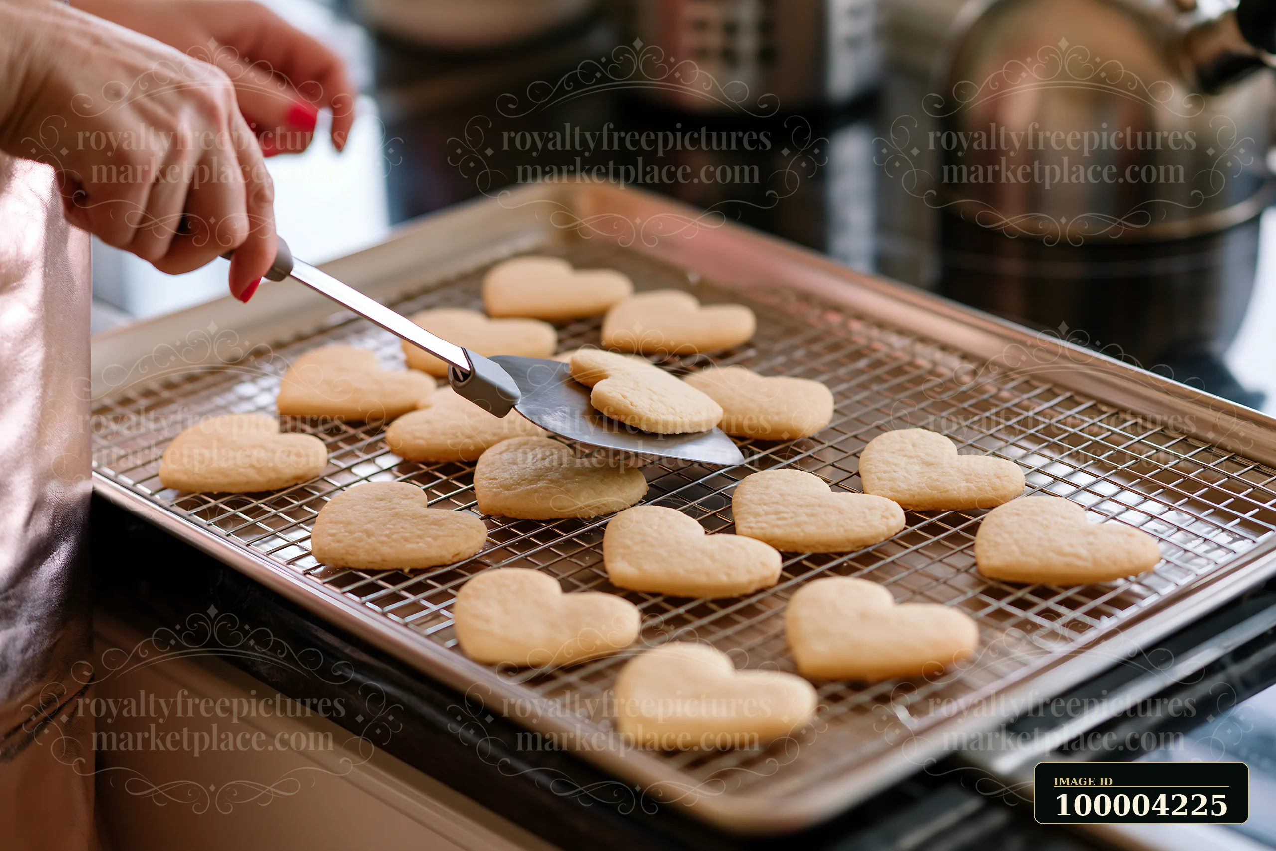 Heart shaped cookies cool on a wire rack as a person lifts one with a spatula.