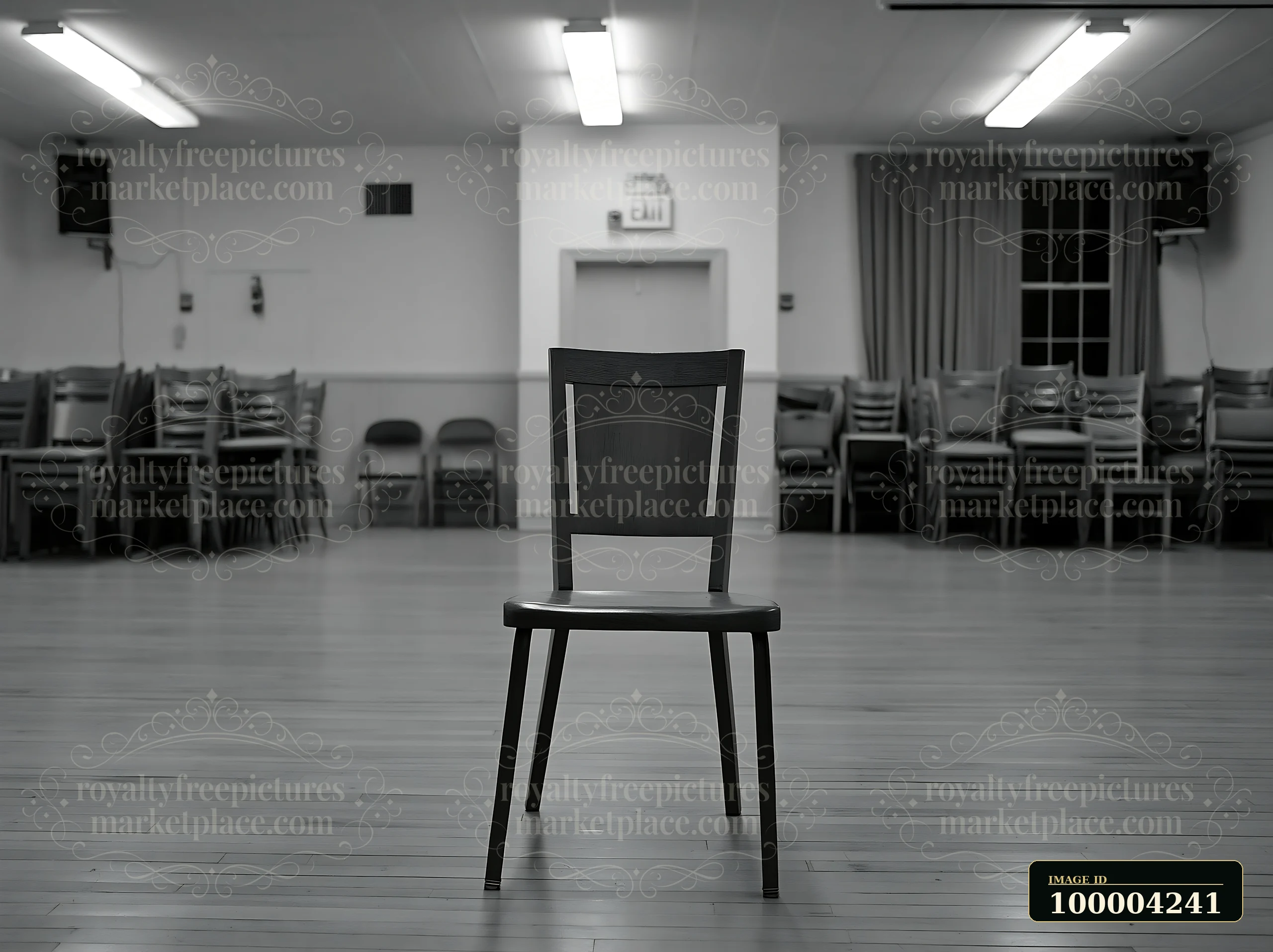 Empty black chair centered in a quiet hall with stacked chairs and a somber atmosphere.