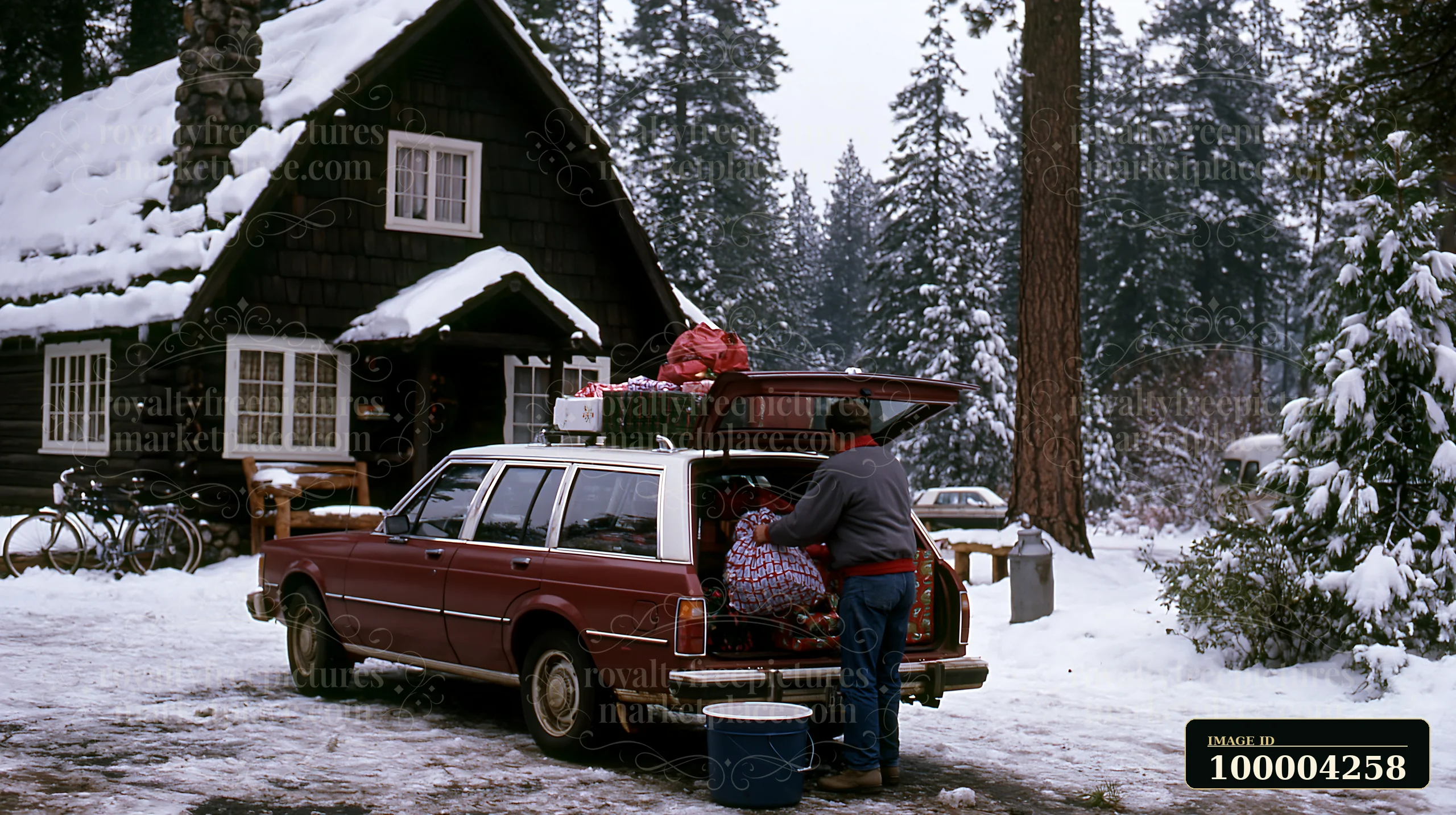 A person packs the trunk of a car with holiday items outside a cabin in a snowy forest.