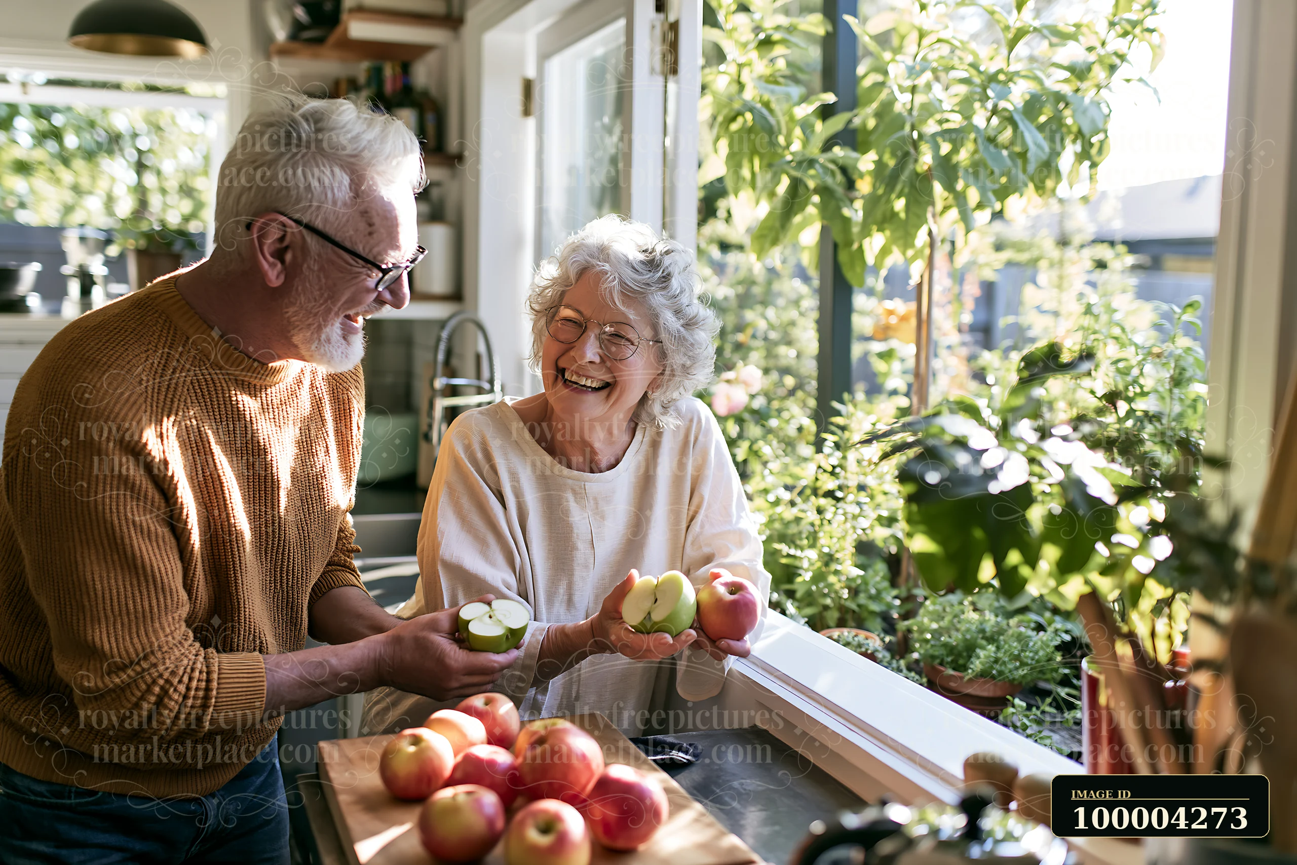Elderly couple laughing together while holding apples in a bright kitchen beside a sunny window.