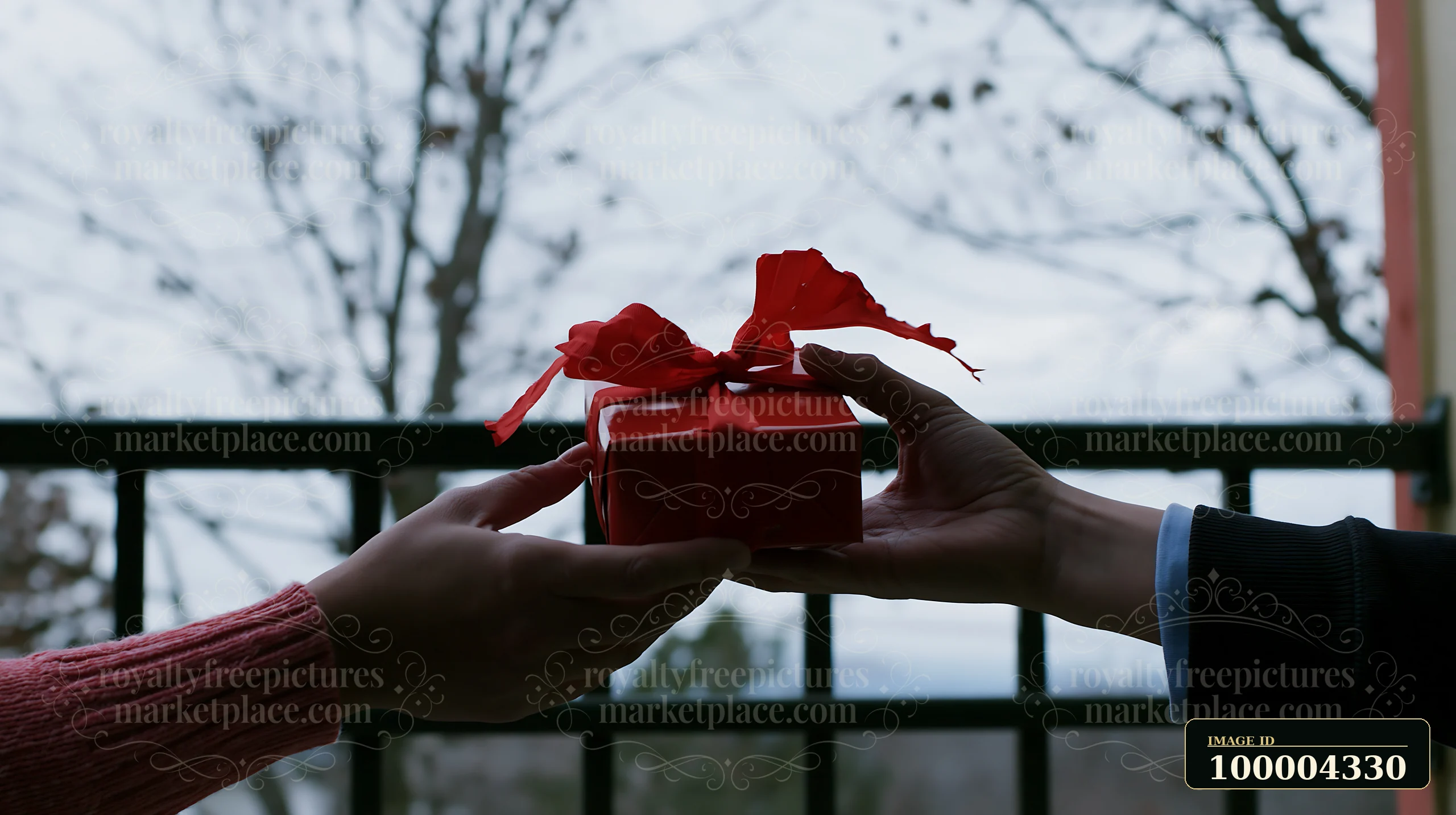 Two hands are seen exchanging a red gift with a bow while cold weather is visible in the background.