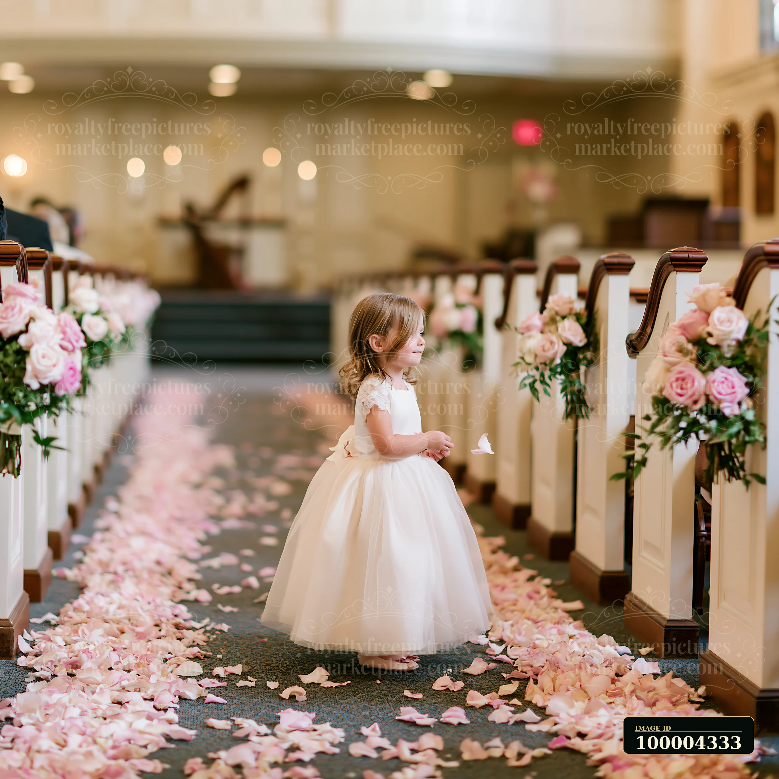 Young flower girl in a white dress walks through a church aisle covered with pink petals.