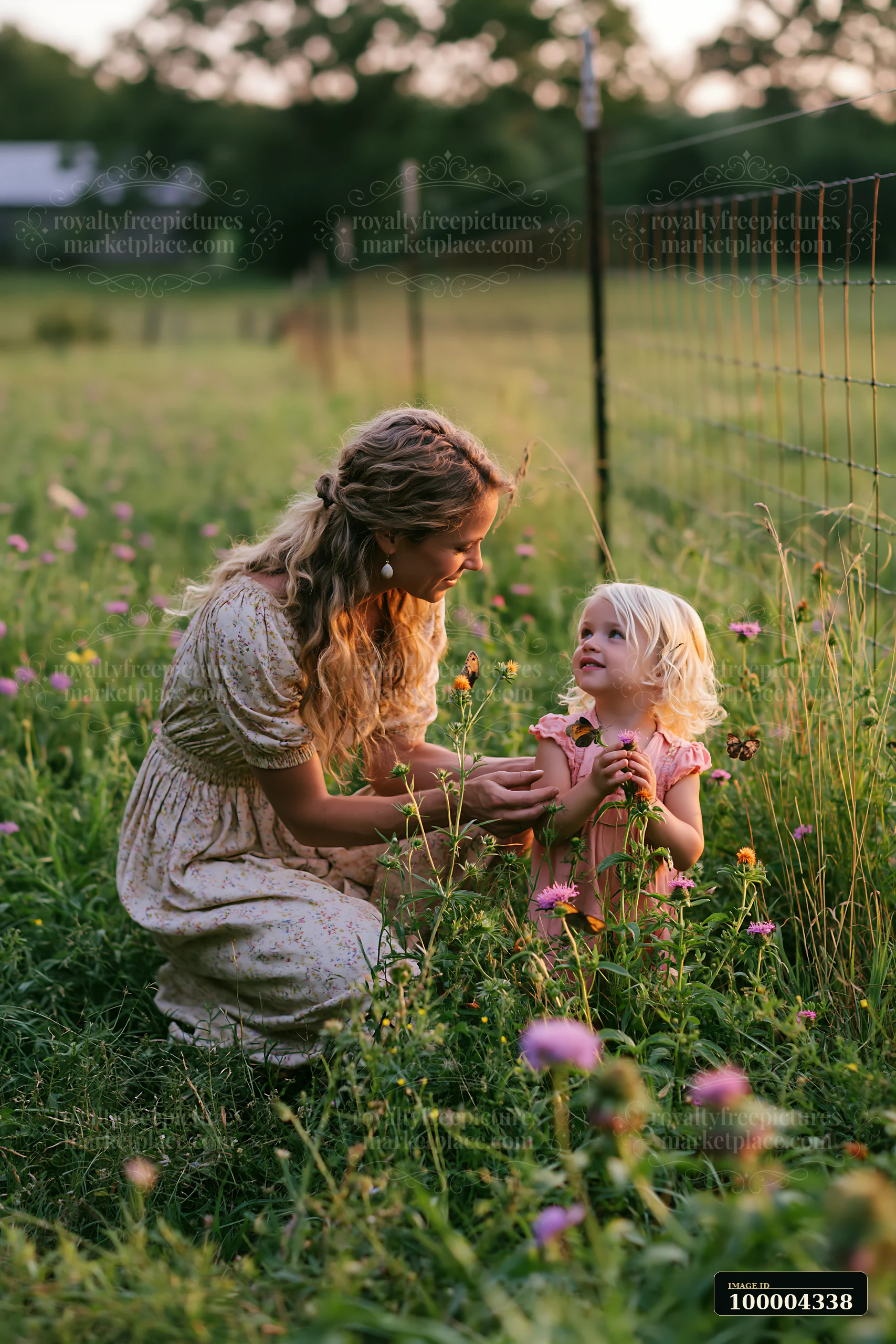 Mother and daughter explore wildflowers in a meadow beside a wire grazing fence.