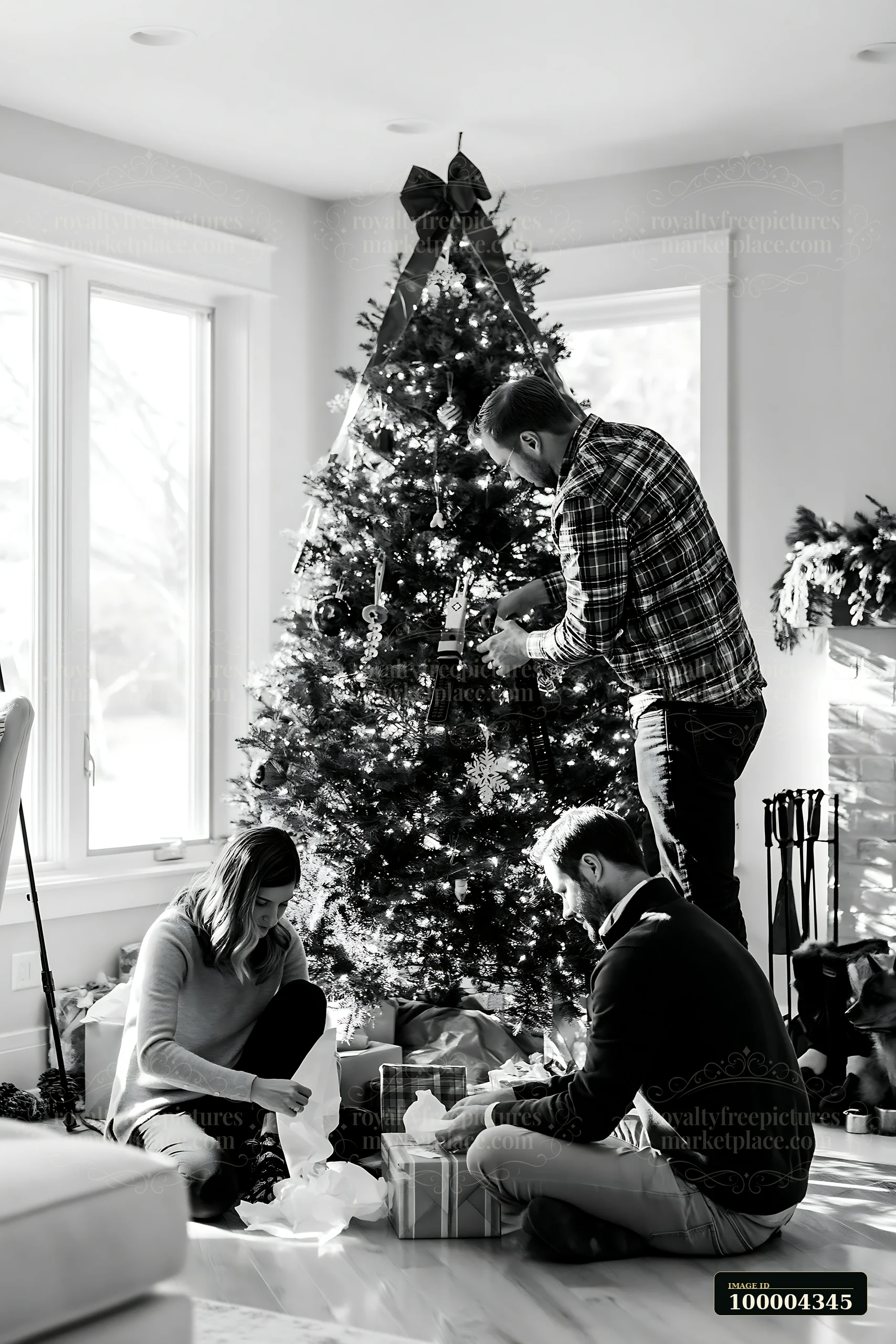 Three adults decorate a lit Christmas tree while opening wrapped gifts in a bright living room.
