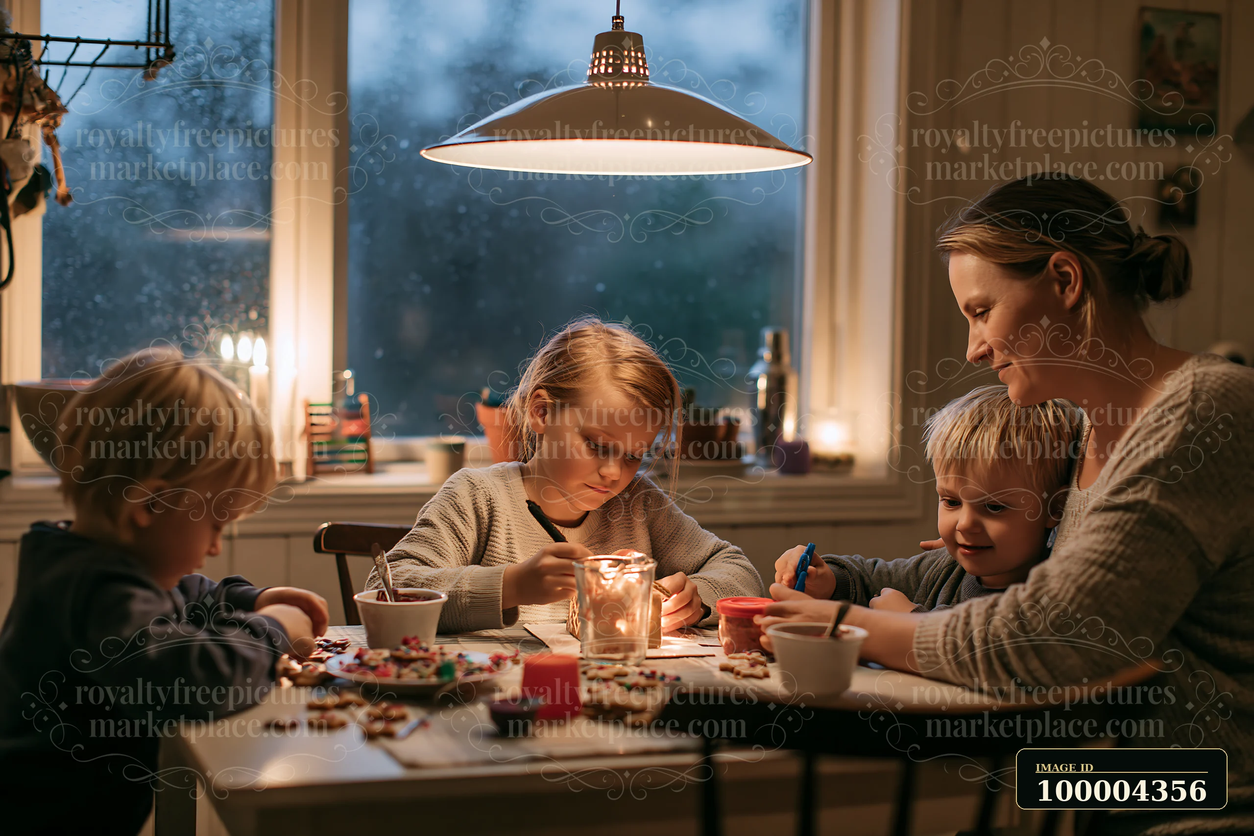 A family is assembling a gingerbread house at a table during a cozy evening.
