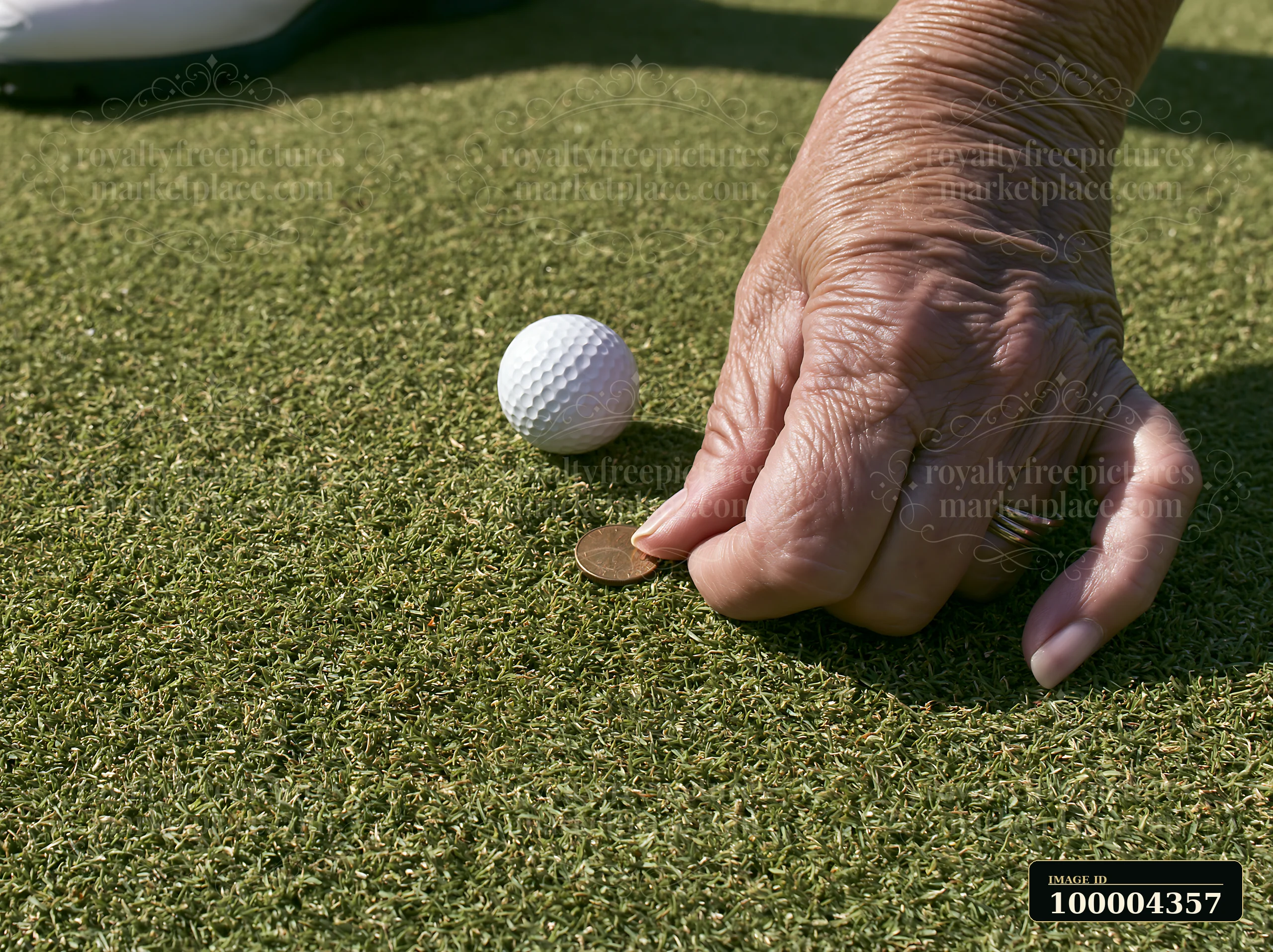 A senior woman places a coin next to a golf ball on a putting green.