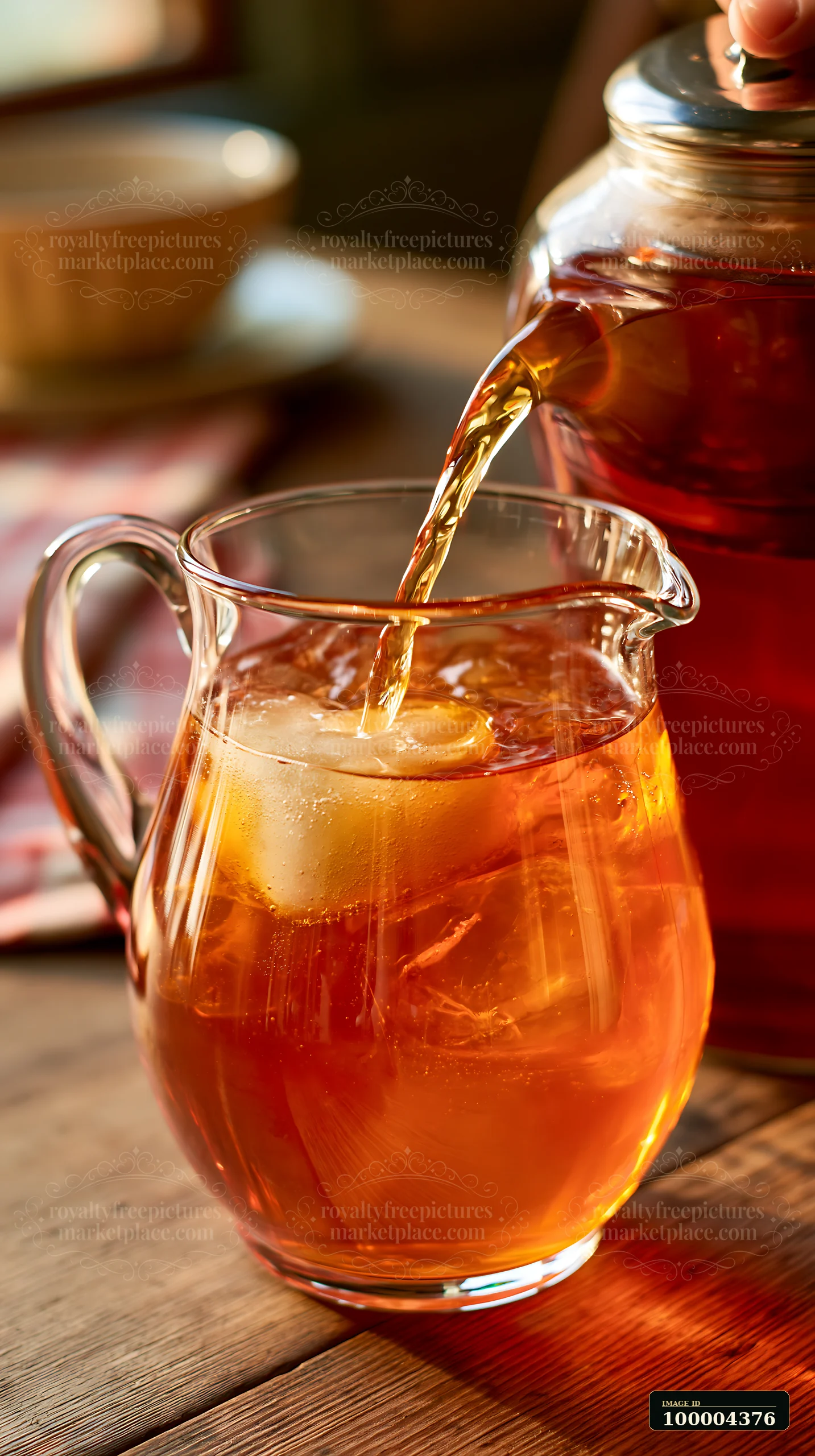 Amber iced drink pours into a glass pitcher with ice on a warmly lit wooden table.