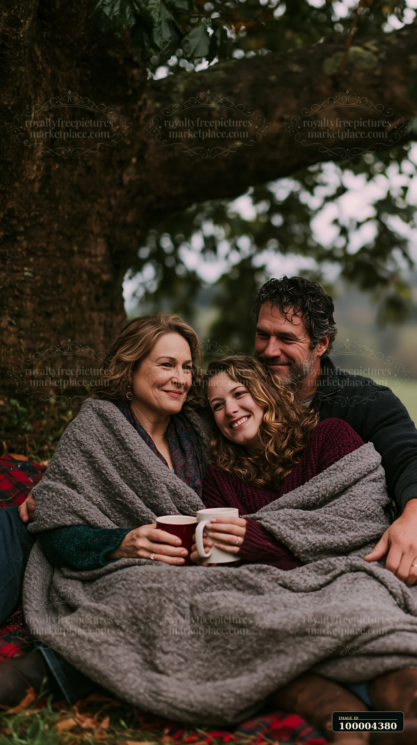 A family sits together under a tree, wrapped in warm blankets and enjoying each other's company.