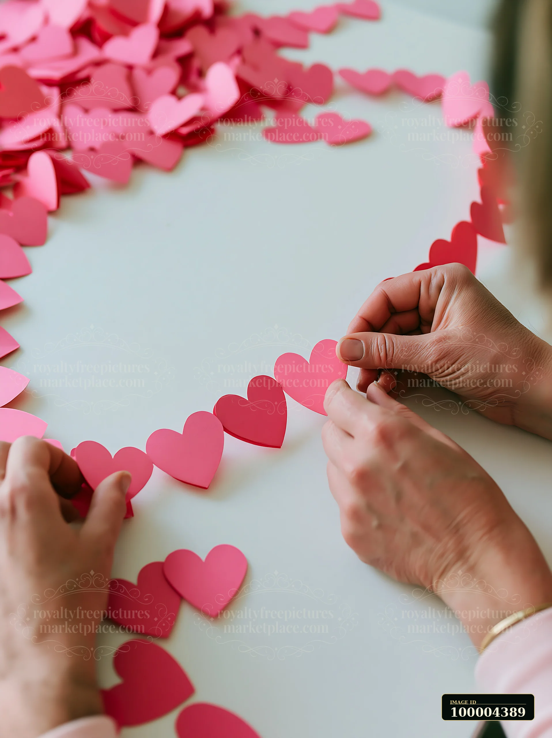 Two people arrange pink paper hearts scattered on a white table.