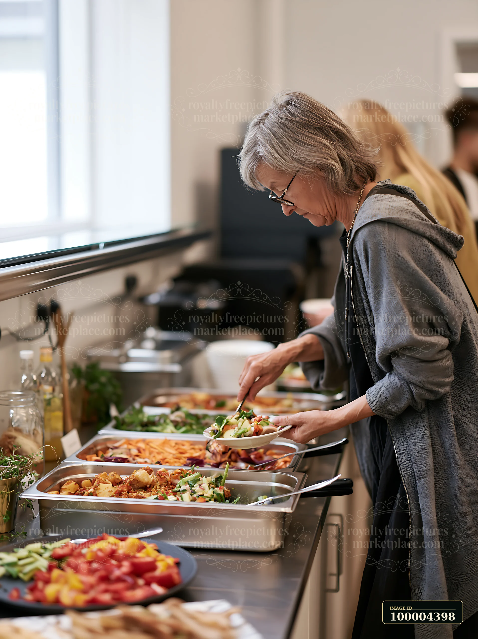 Woman serving salad from a tray at a casual office lunch buffet with prepared dishes on an indoor counter.