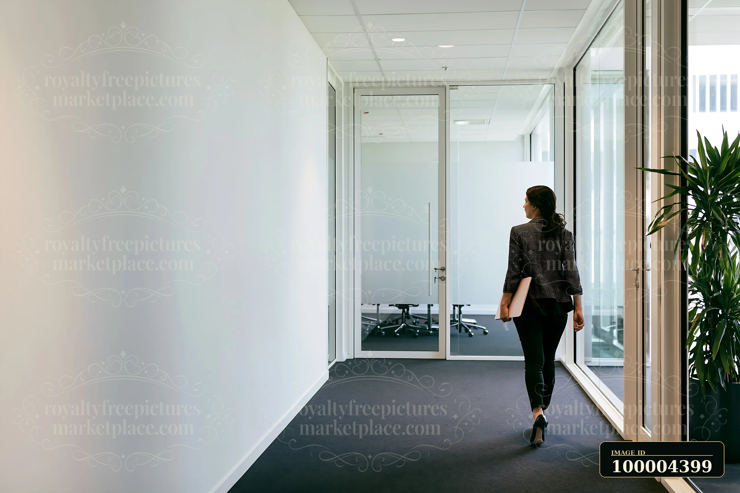 A businesswoman walks through a modern office corridor while holding a folder.