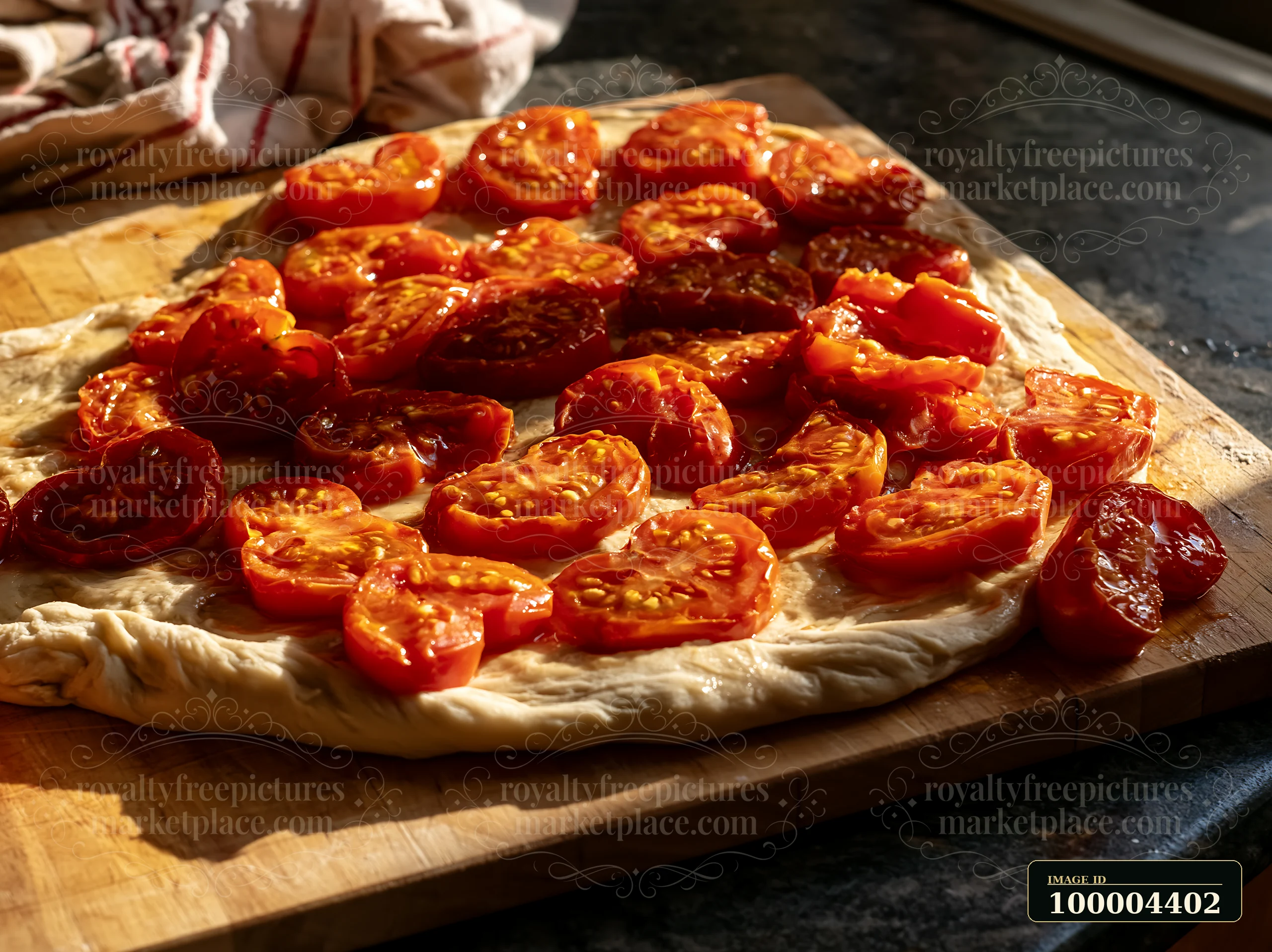 Tomato slices arranged on dough atop a wooden cutting board in warm kitchen light.