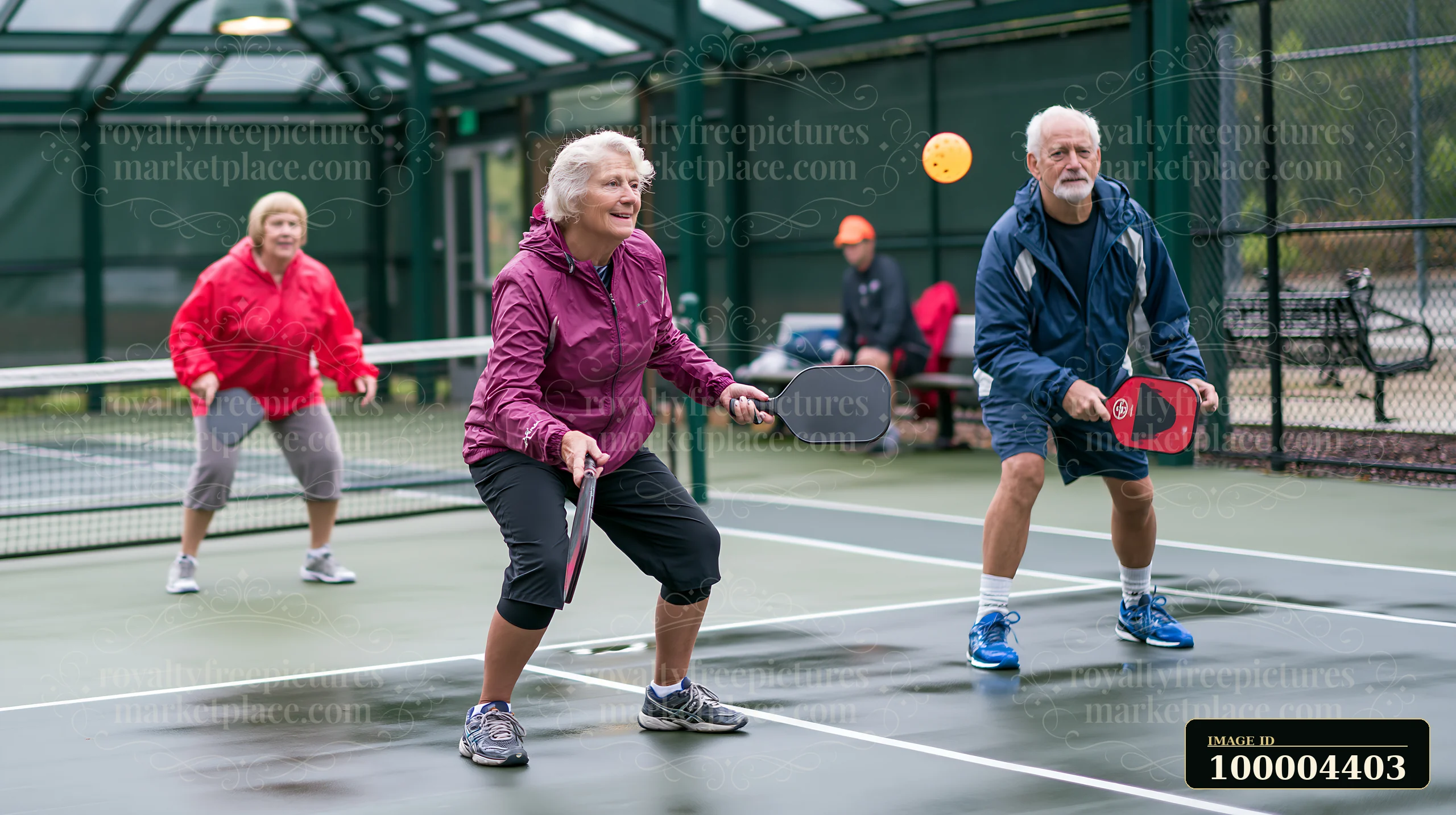 Three older friends engage in a game of pickleball at a recreational court.