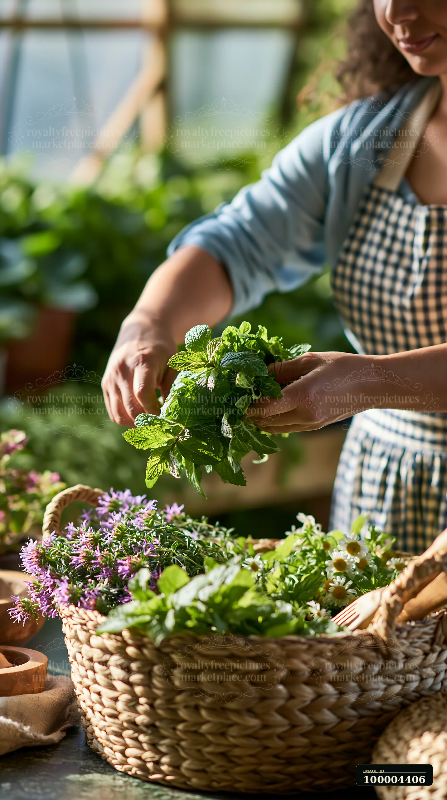 Woman arranging fresh herbs beside meadow flowers in handwoven baskets inside a sunlit greenhouse.