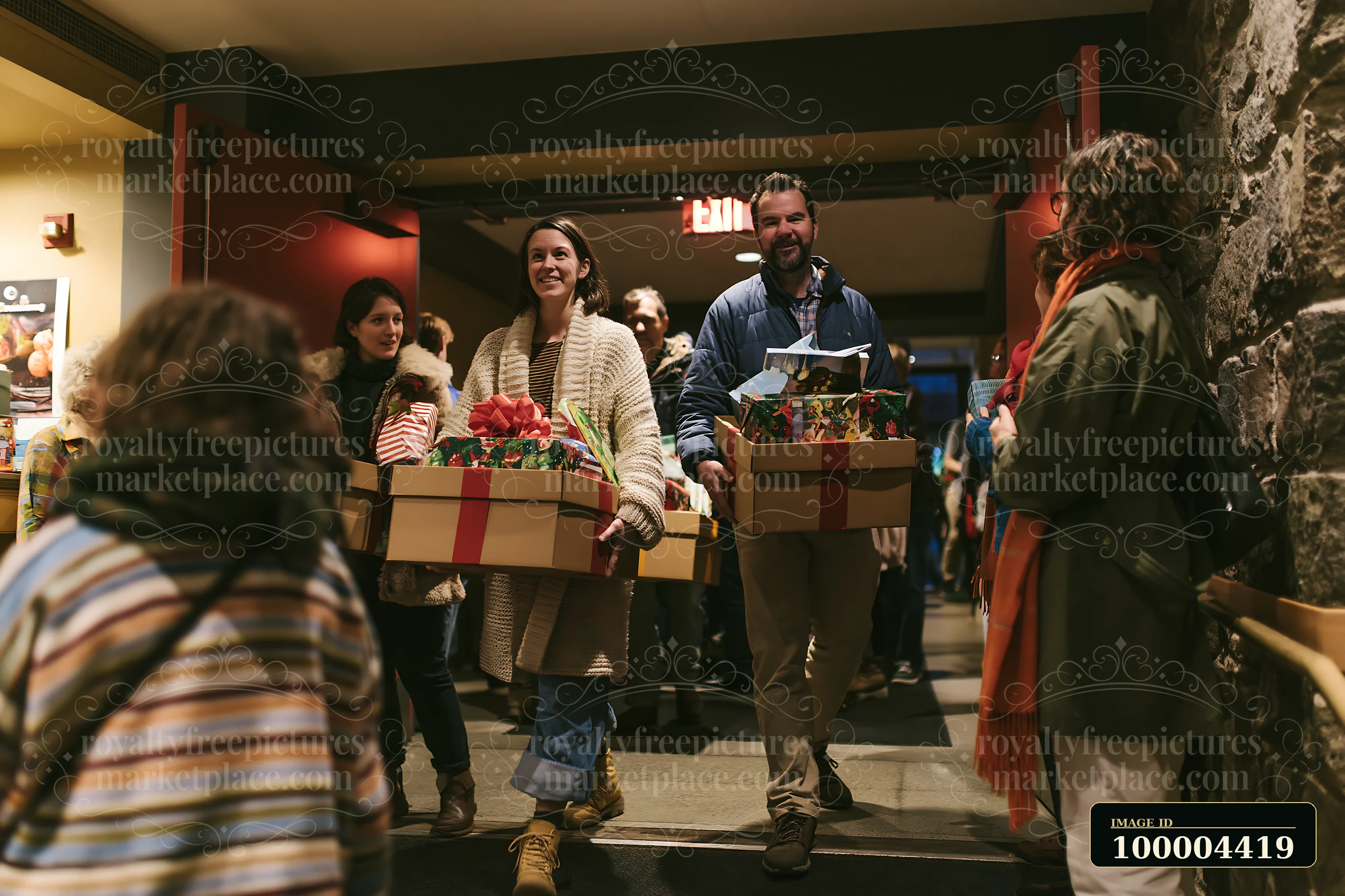 Parents carry decorated gift boxes through a warmly lit indoor hallway surrounded by other people.