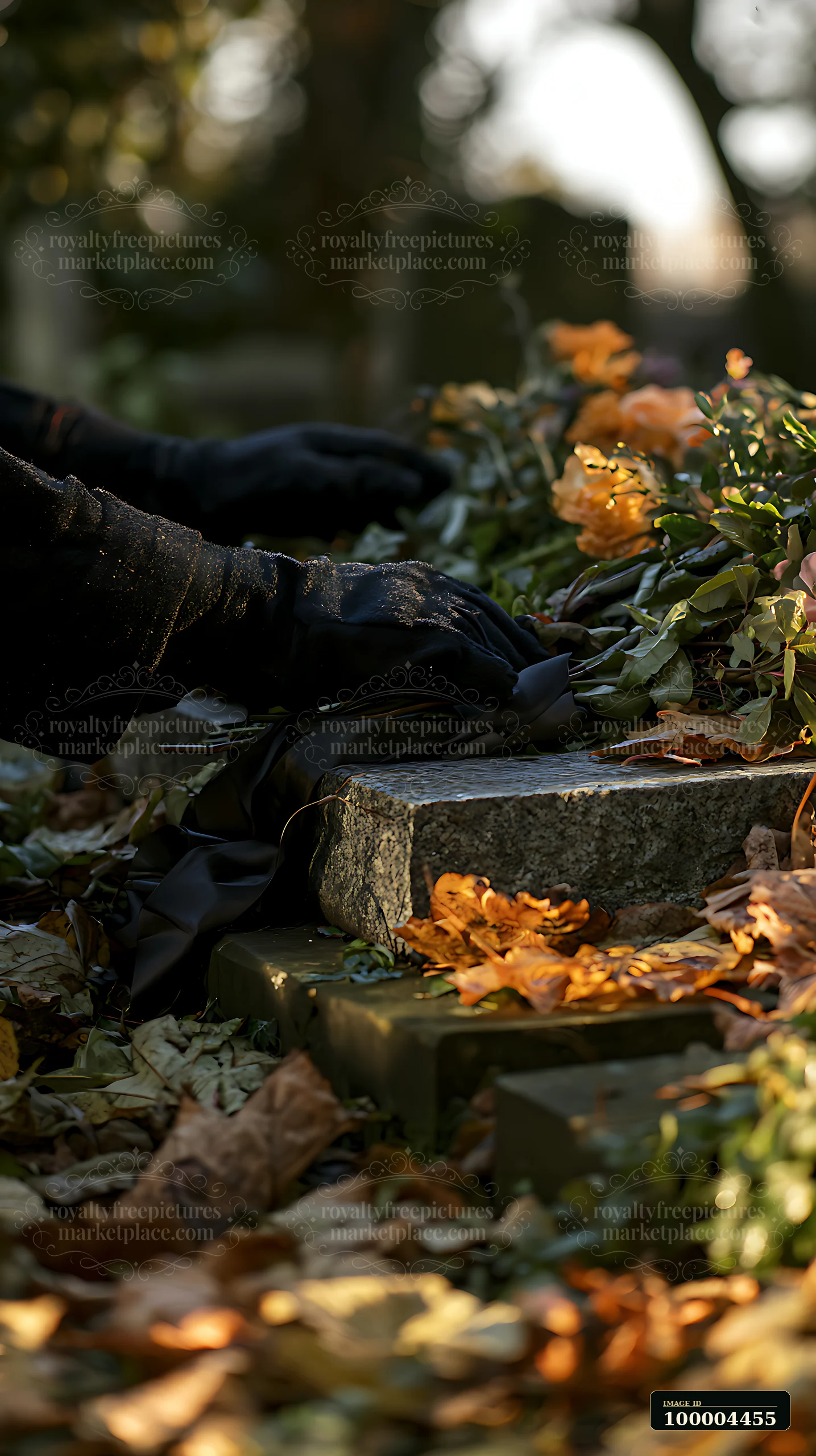 A person in black gloves places a mourning ribbon on a grave surrounded by autumn leaves and flowers.