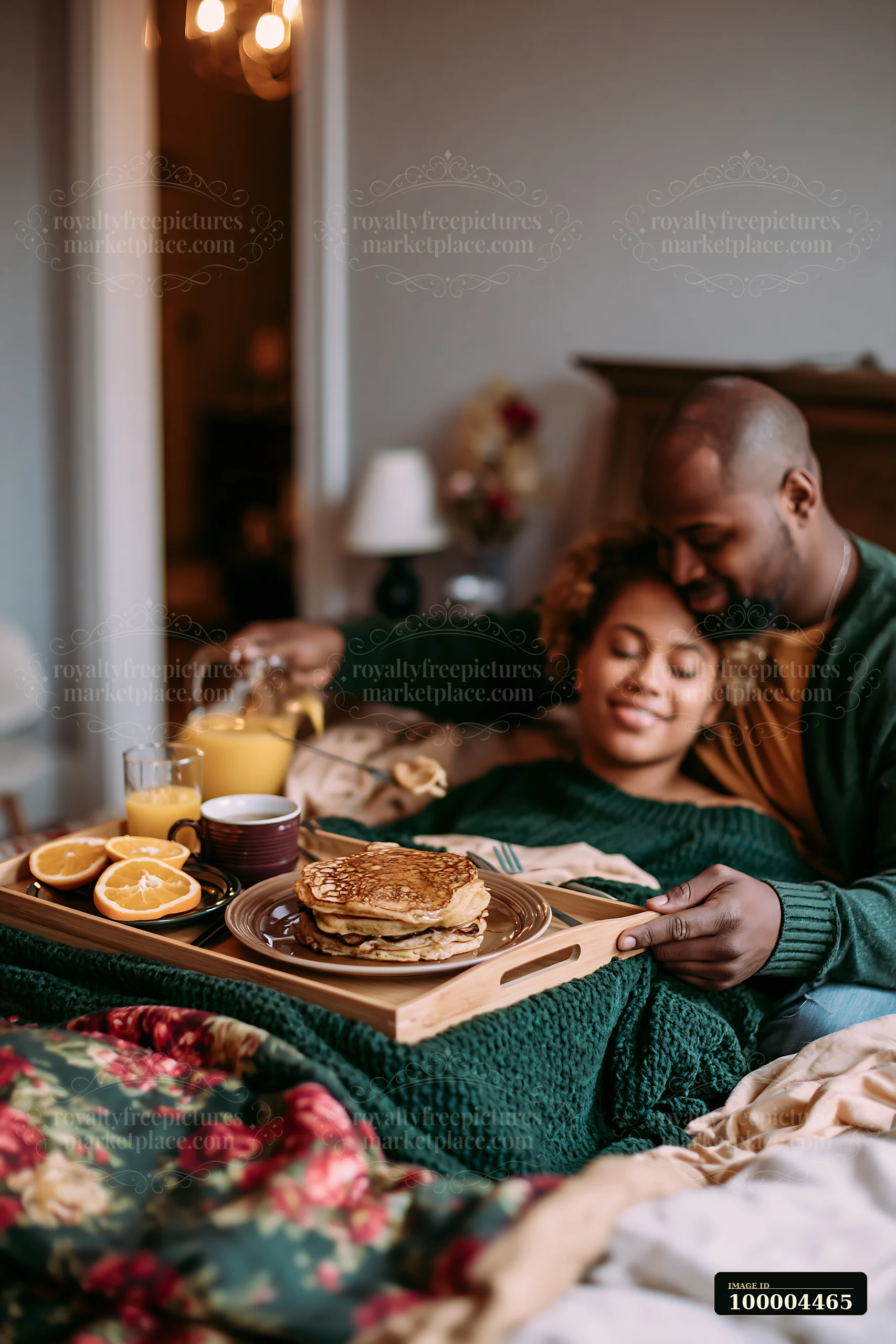 Couple enjoying pancakes, oranges, and juice on a Christmas breakfast tray in bed.