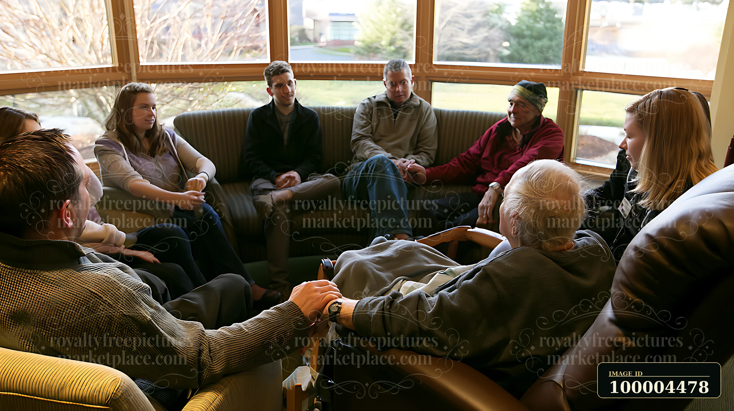 A family sits together in a living room, holding hands while gathered around a hospice patient seated in a chair.